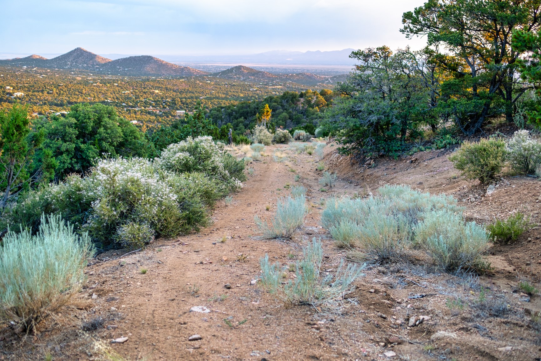 Rocky hillside path overlooks wooded hills and distant mountains across a broad valley.