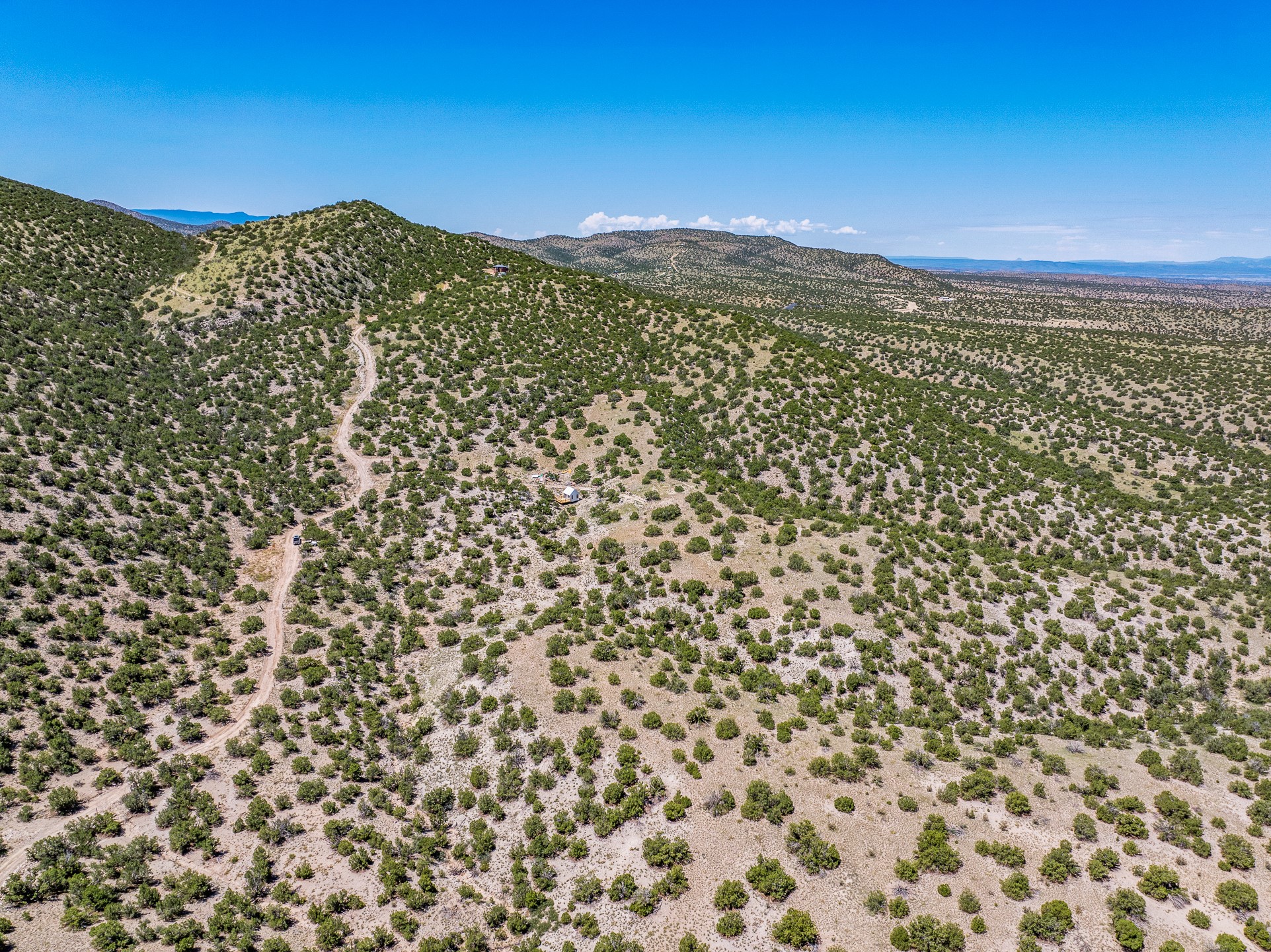 Aerial view of scrub-covered hills with a winding dirt road and a small building.