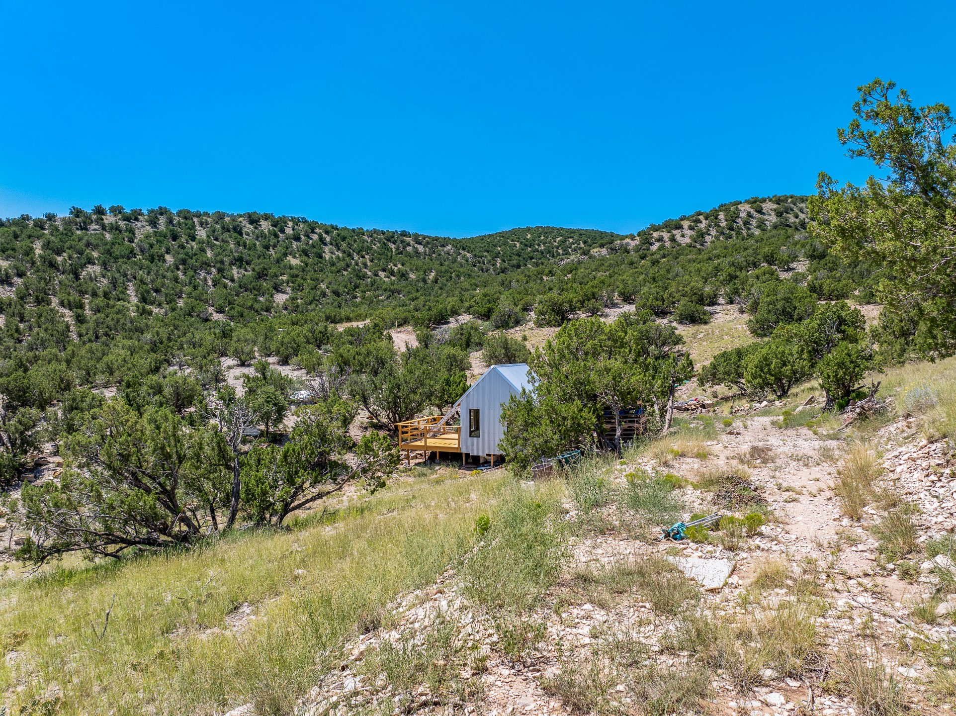 Small white cabin with a wooden deck on a rugged, tree-covered hillside.