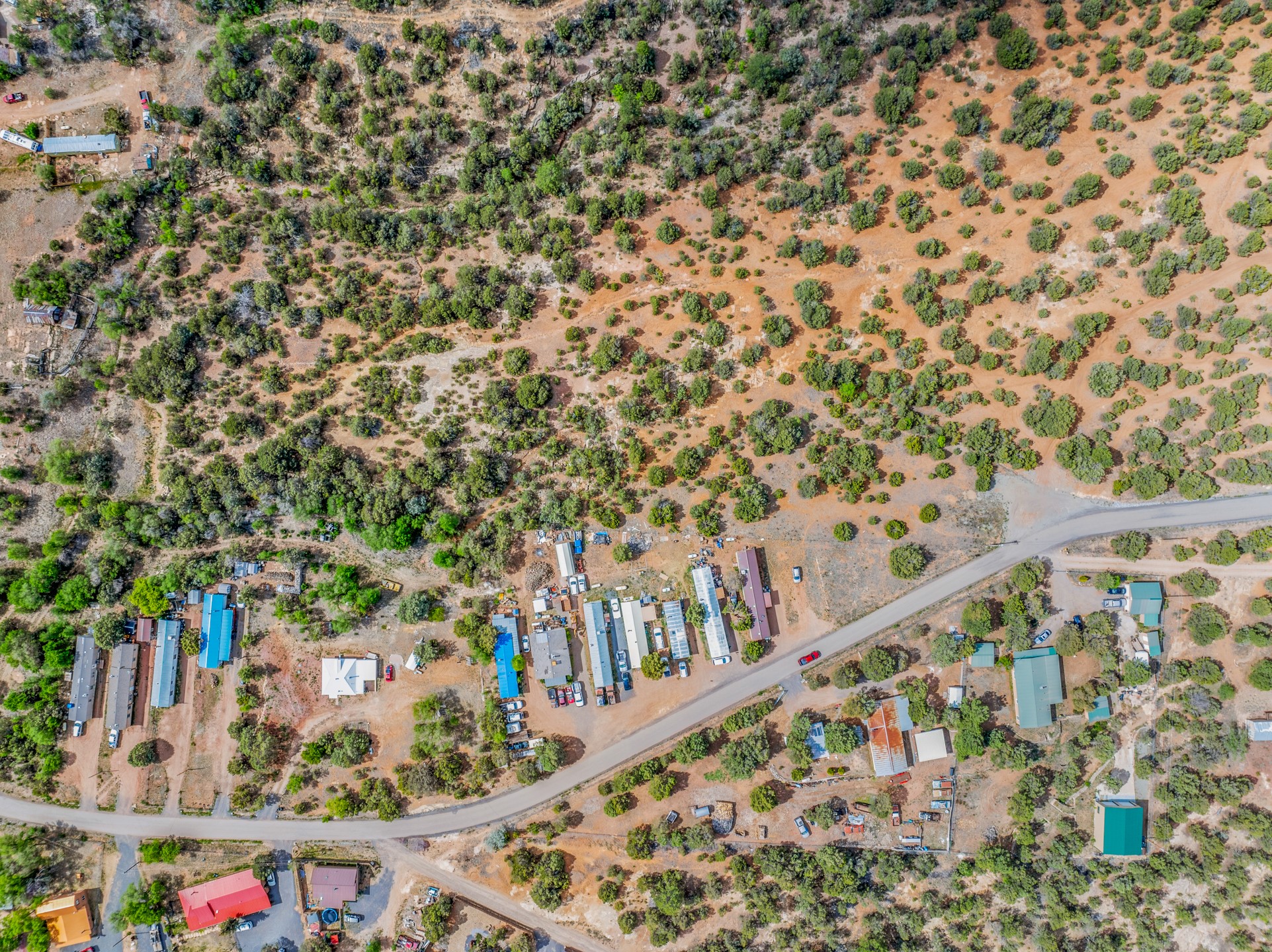Aerial view of scrub-covered acreage beside a curving paved road and scattered buildings.