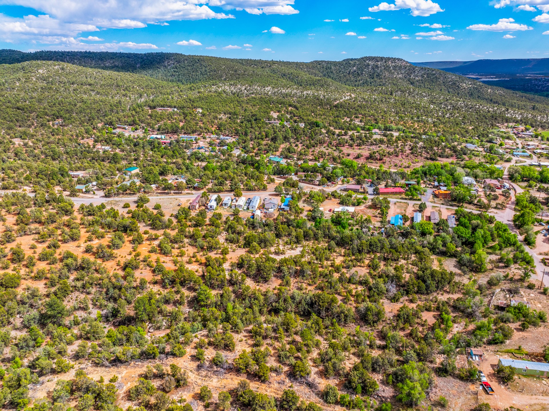 Aerial view of wooded acreage and scattered homes below forested hills.