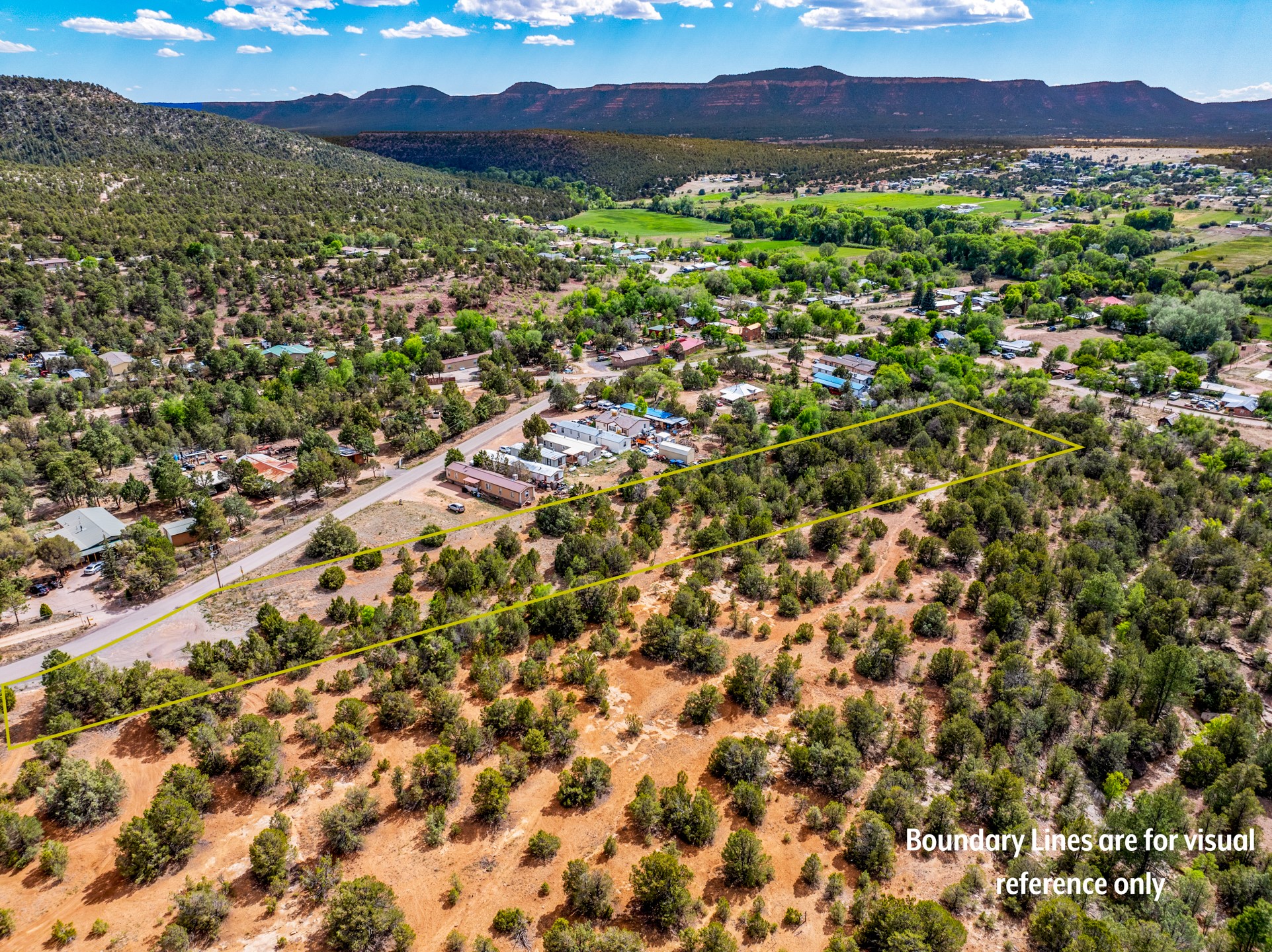 Aerial view of a wooded parcel outlined in yellow, with a road, nearby homes, and distant mesas.