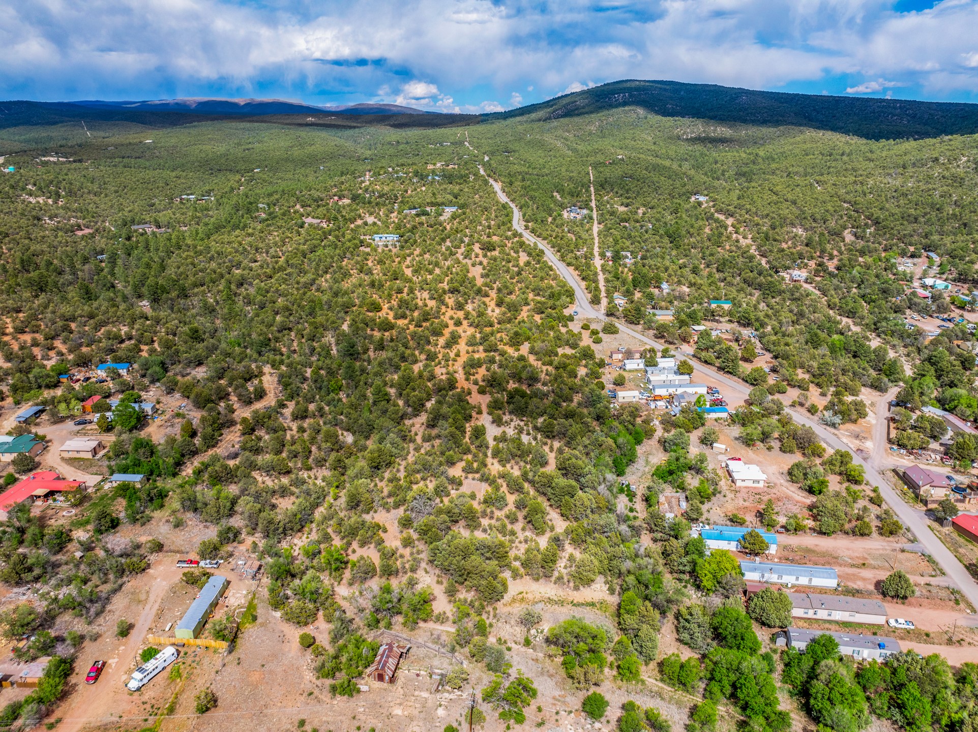 Aerial view of wooded, sparsely developed land with scattered homes, winding roads, and distant mountain ridges.