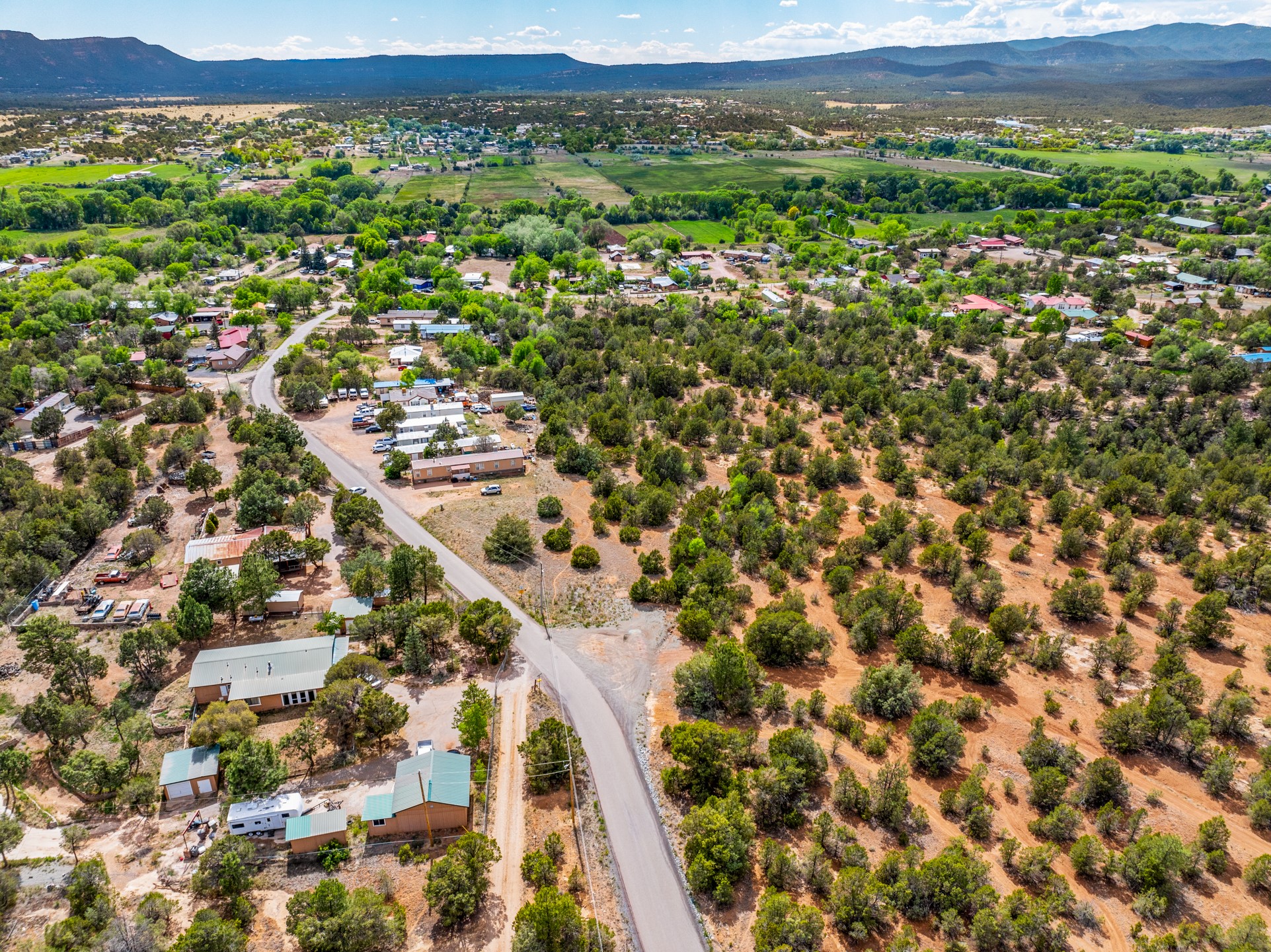 Aerial view of scrub-covered land beside a rural road, with nearby homes and mountains beyond.