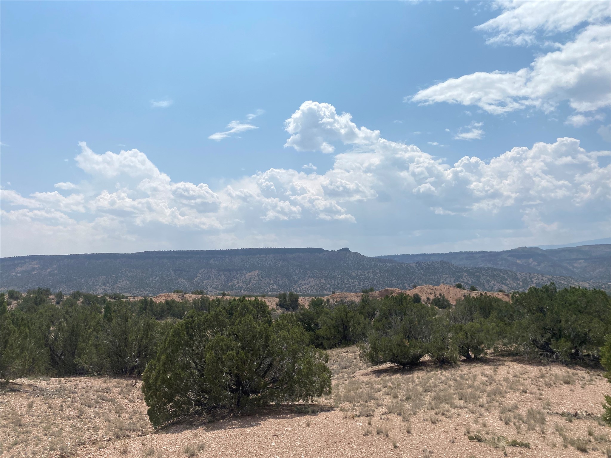 Dry, shrub-covered land with distant ridges beneath a blue sky filled with clouds.