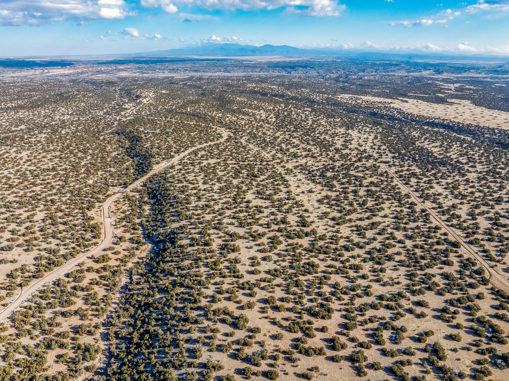 Aerial view of desert acreage with winding dirt roads and distant mountains.