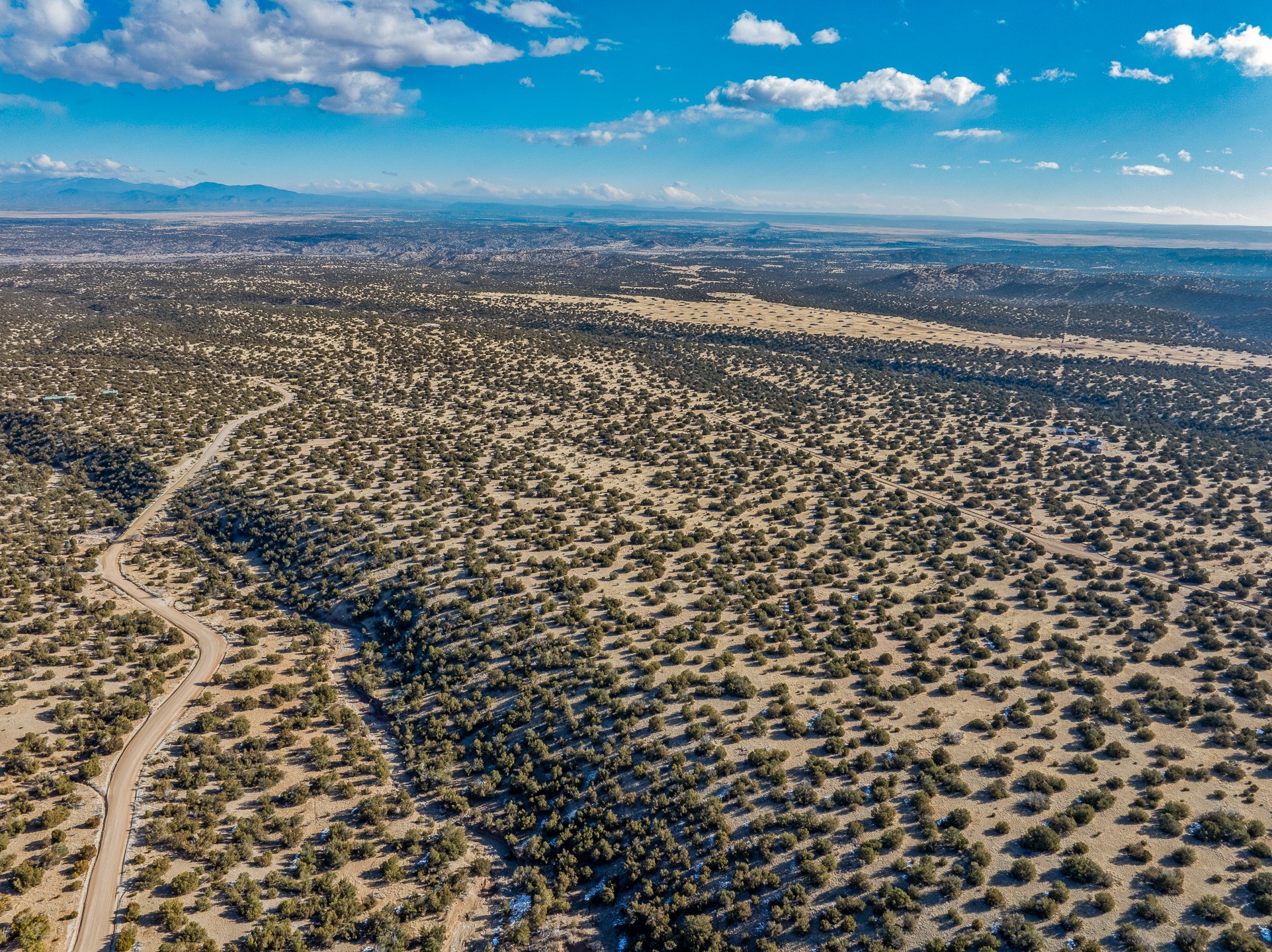 Aerial view of scrubland with a winding dirt road and distant mountains.