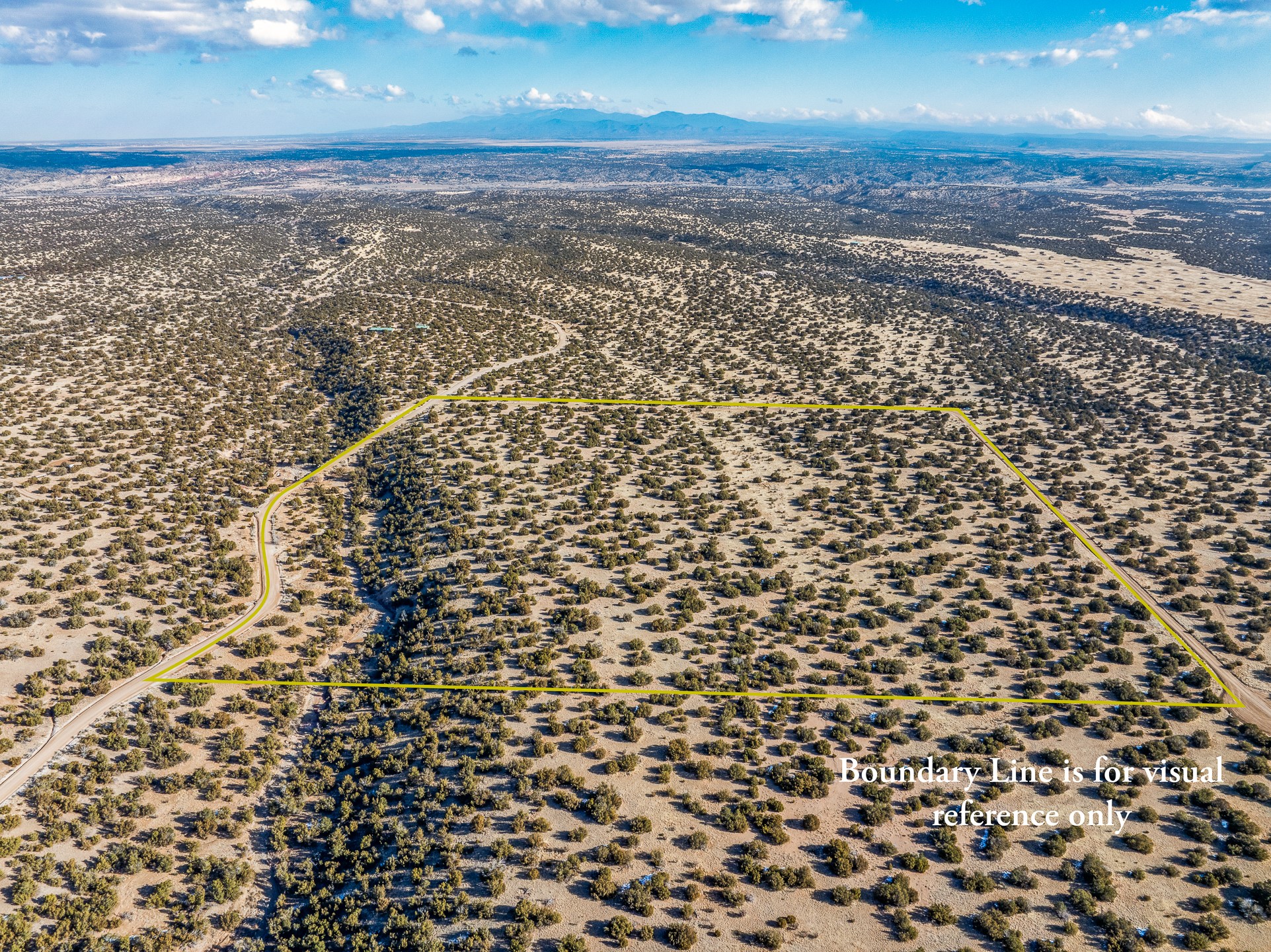 Aerial view of scrub-covered vacant land outlined in yellow, with a dirt road and distant mountains.