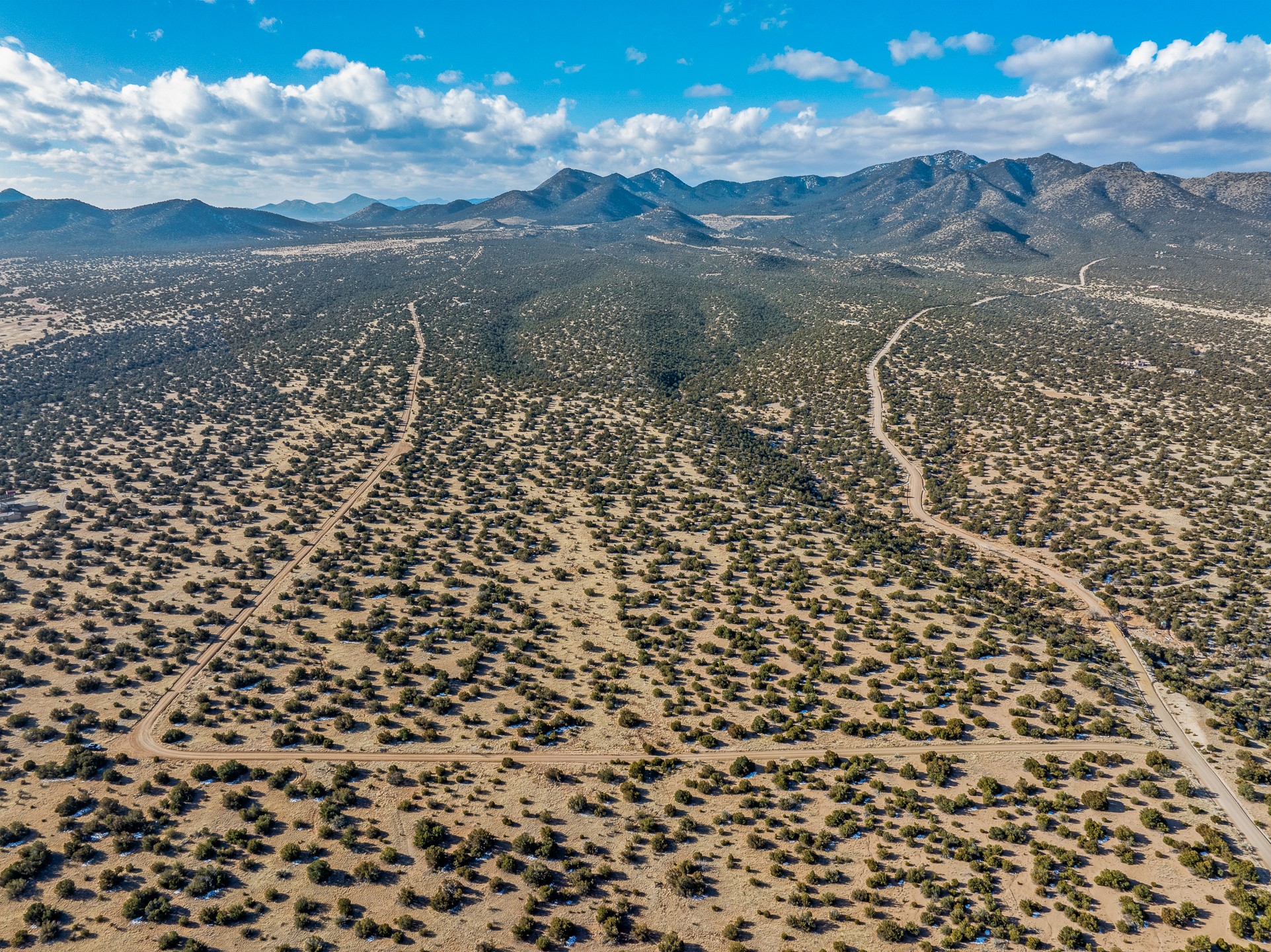 Aerial view of desert scrubland with dirt roads and mountains in the distance.