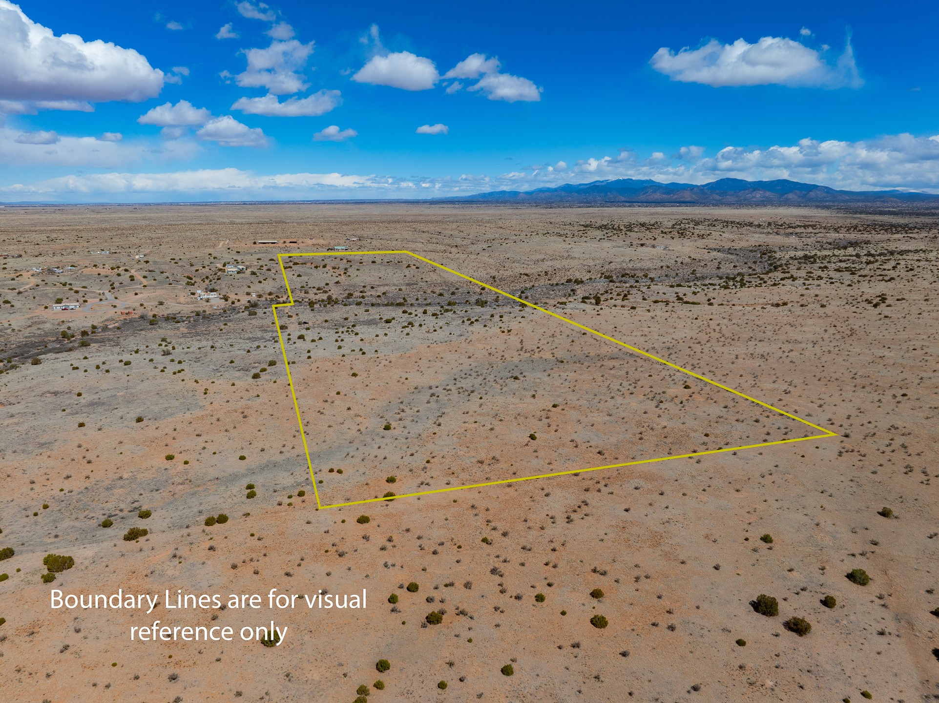 Aerial view of a vacant desert parcel outlined in yellow, with sparse shrubs and distant mountains.