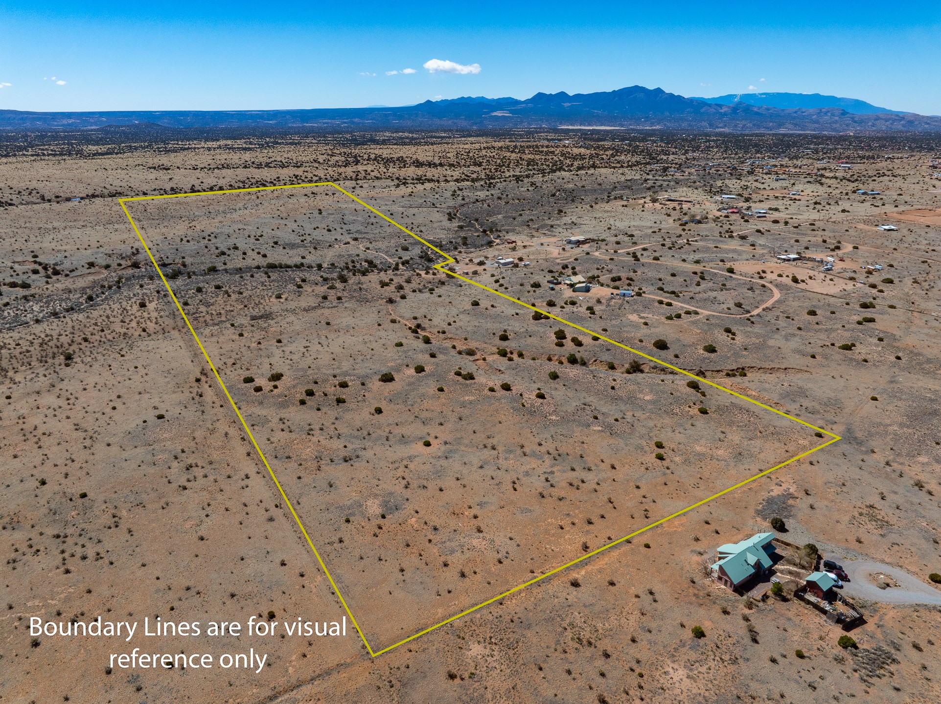 Aerial view of scrub-covered land outlined in yellow, with nearby homes and mountains beyond.