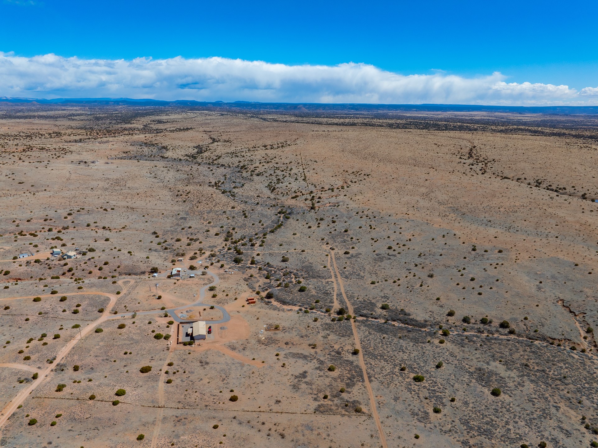 Aerial view of 38 Acres Sundog, with sparse desert scrub, dirt roads, scattered buildings, and distant hills.