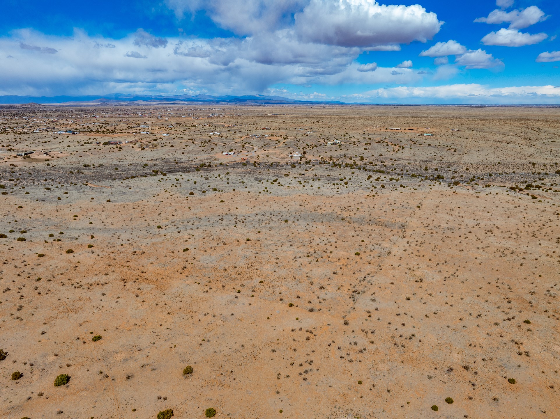 Aerial view of dry, shrub-dotted acreage with distant mountains and scattered buildings on the horizon.