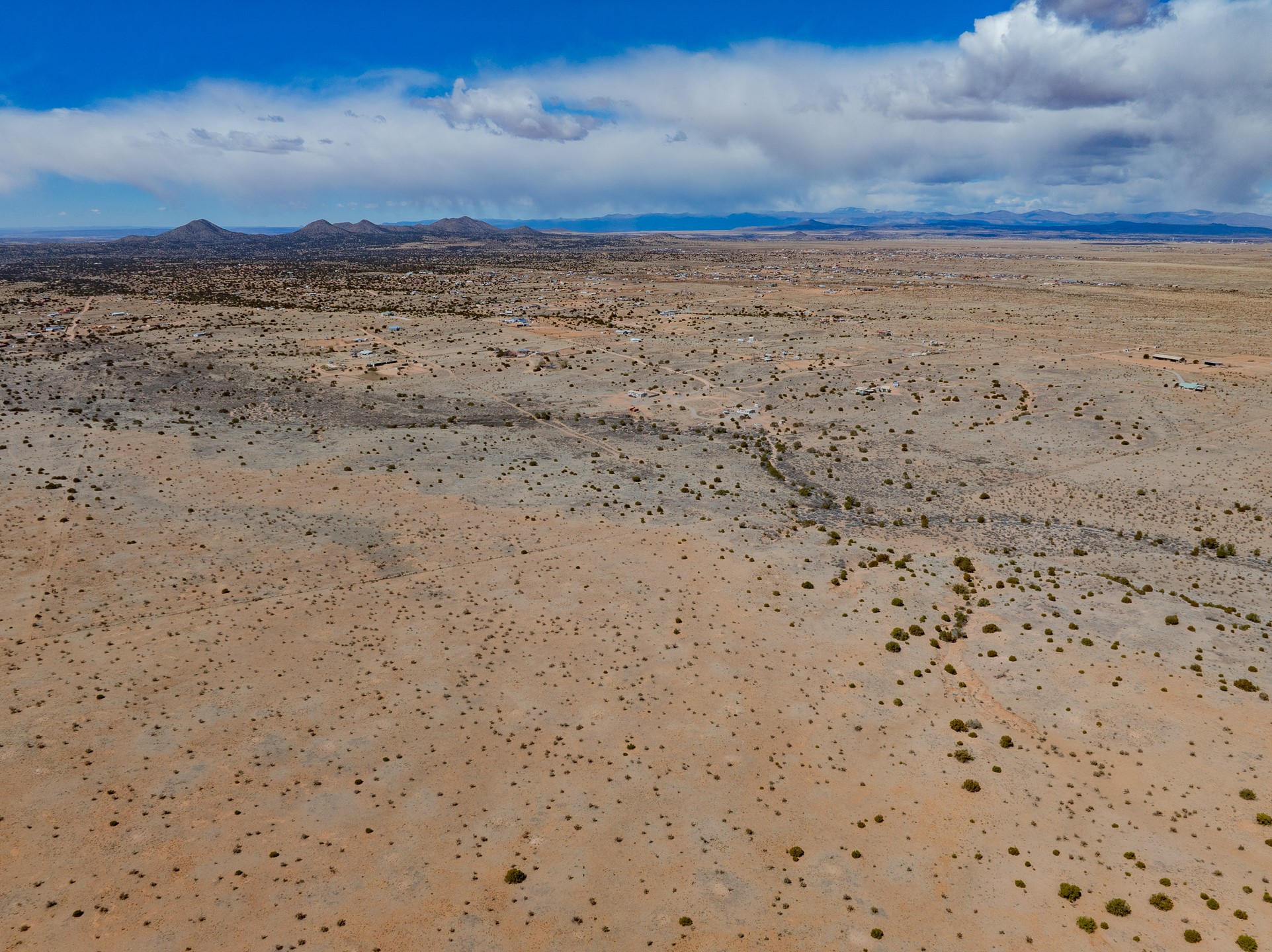 Aerial view of arid, shrub-dotted land with scattered buildings and distant mountains.