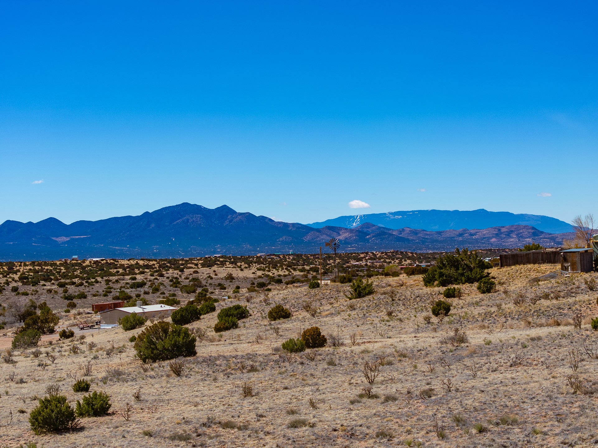 Scrub-covered acreage with a windmill and small outbuilding, backed by distant mountains.
