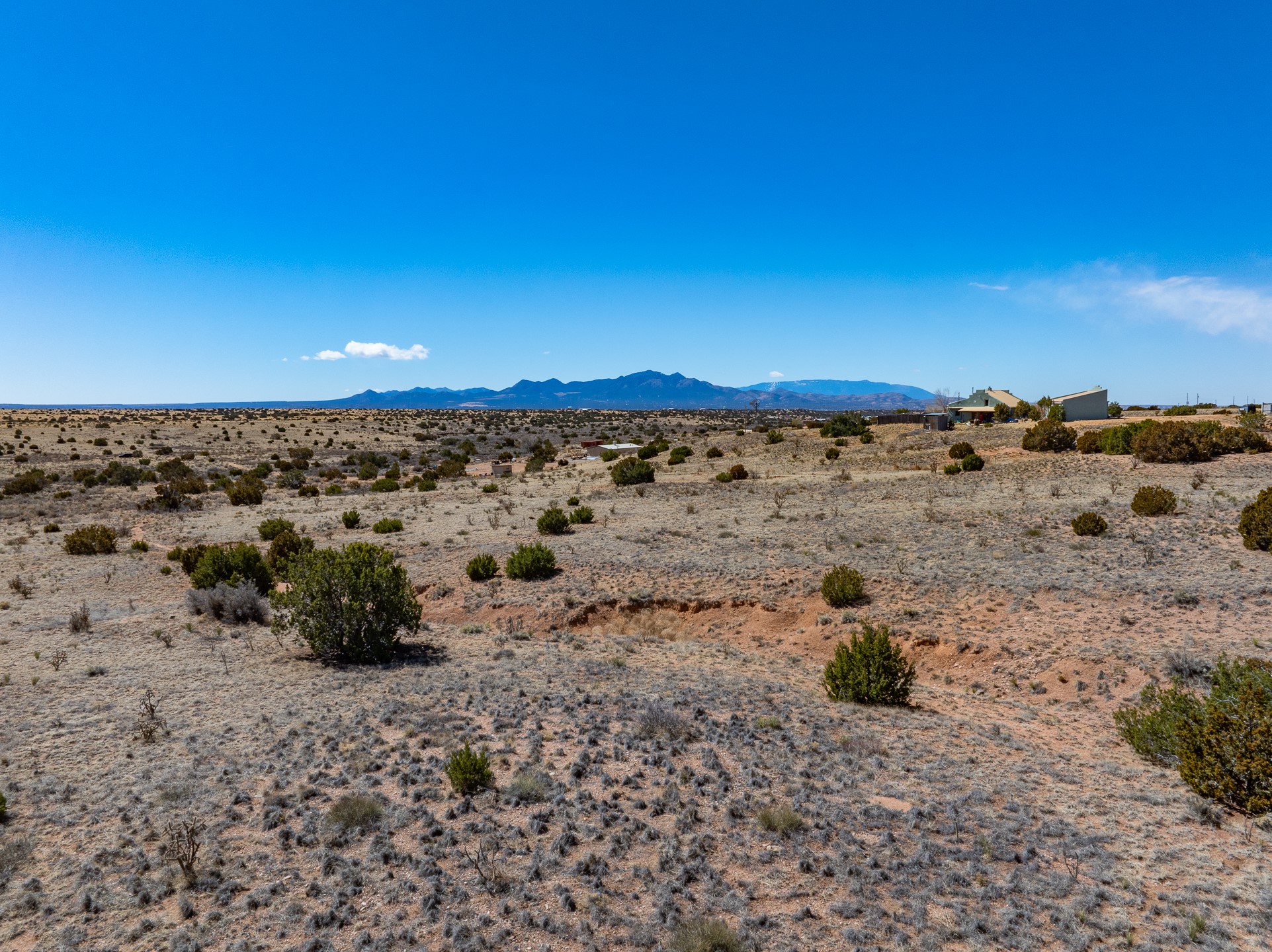 High-desert acreage with scattered shrubs, distant buildings, and a mountain range.