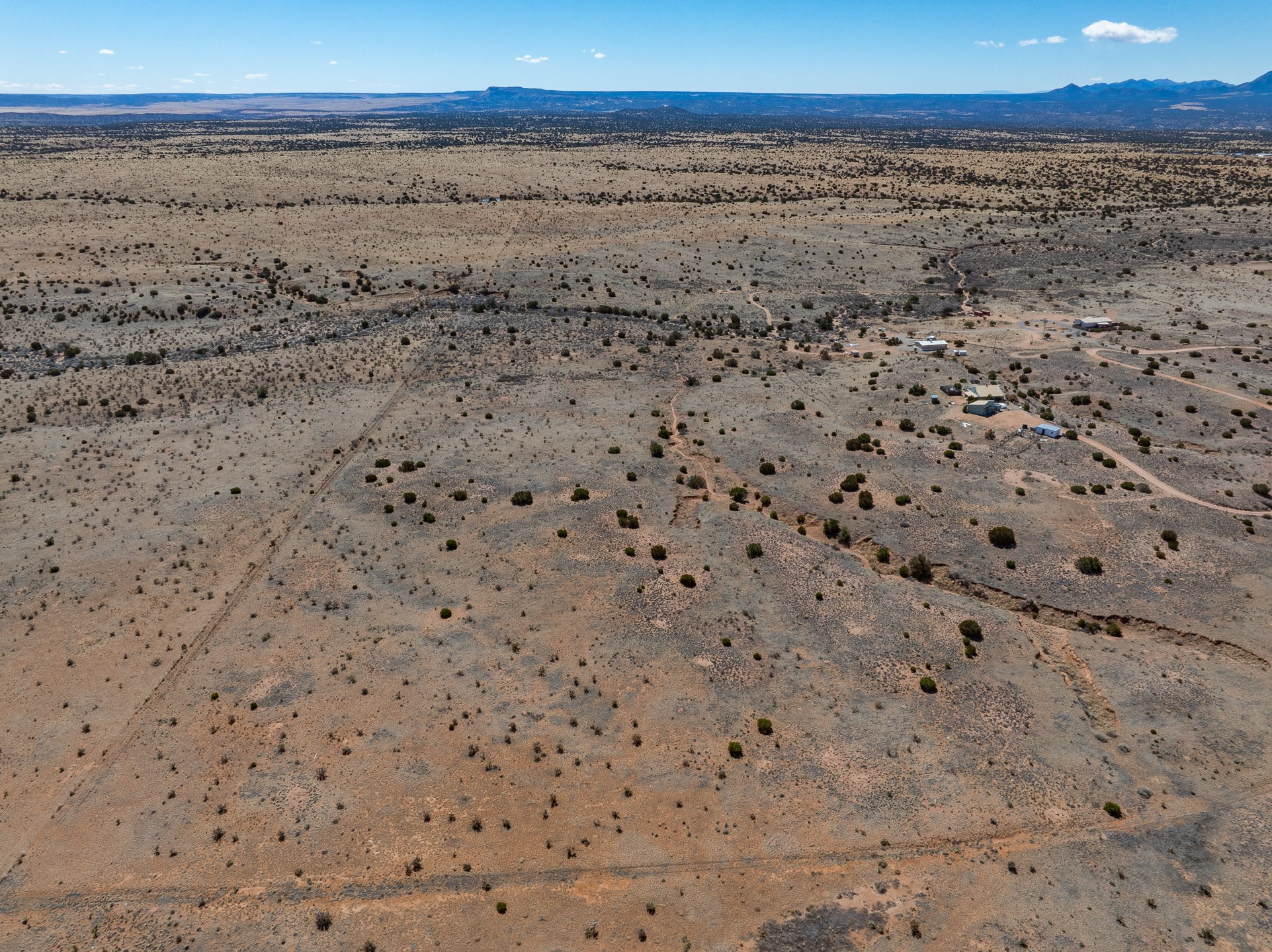 Aerial view of scrubland with scattered buildings, dirt tracks, and distant mountains.