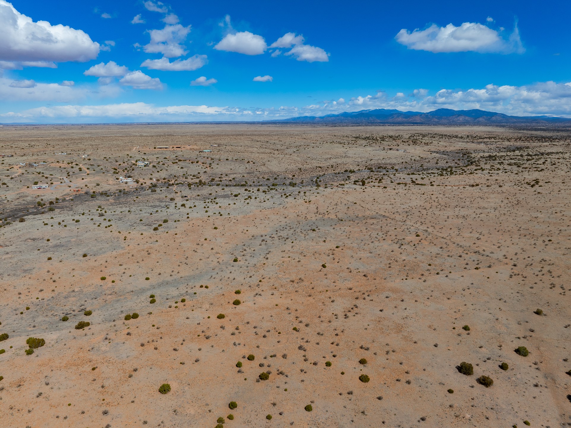 Aerial view of arid, shrub-dotted land with distant buildings and mountains.