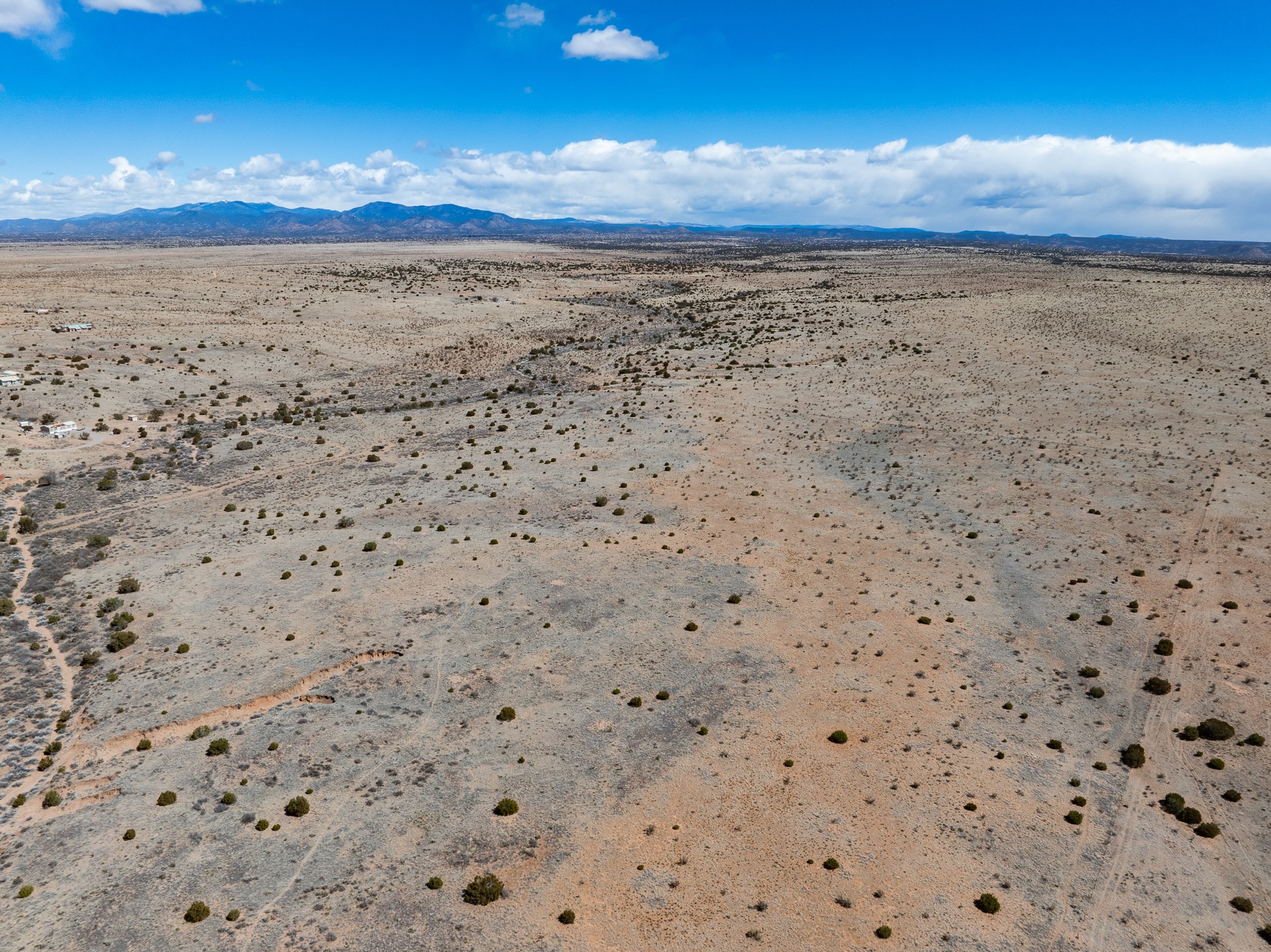 Aerial view of sparse high-desert acreage with faint tracks and mountains on the horizon.