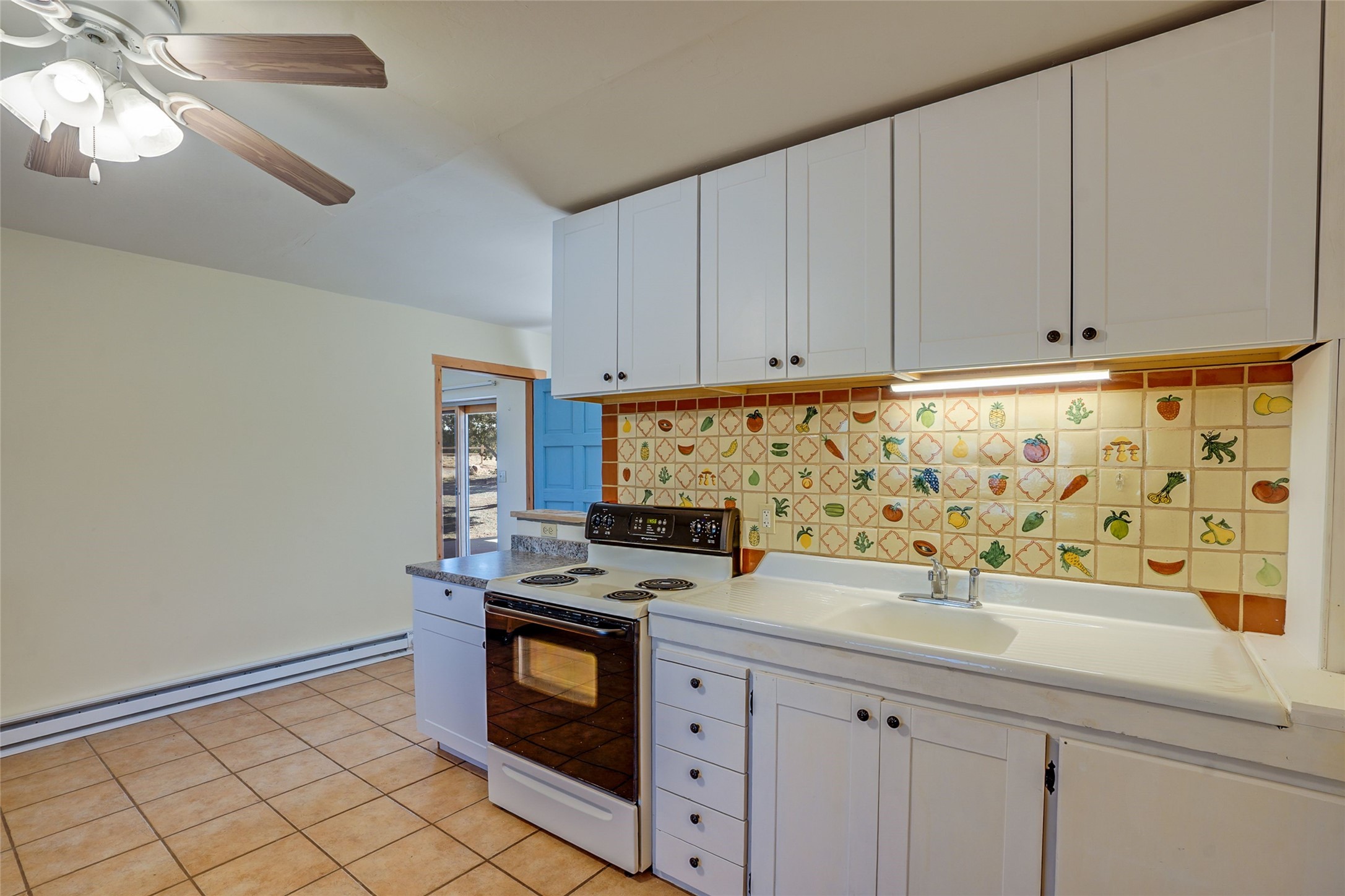 Kitchen with white cabinets, electric range, and colorful fruit-and-vegetable tile backsplash.