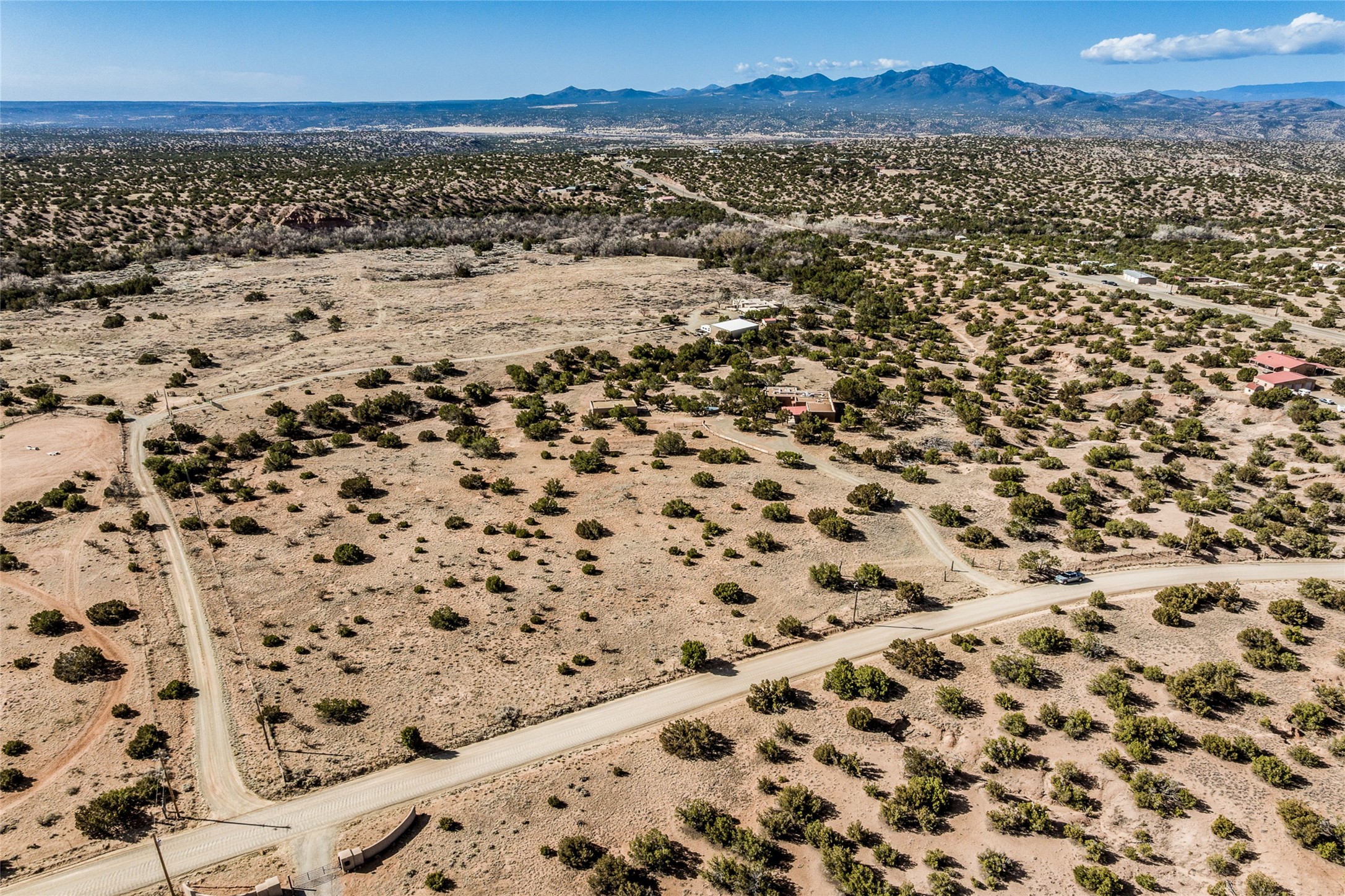 Aerial view of sparsely vegetated desert land, dirt roads, scattered homes, and distant mountains.