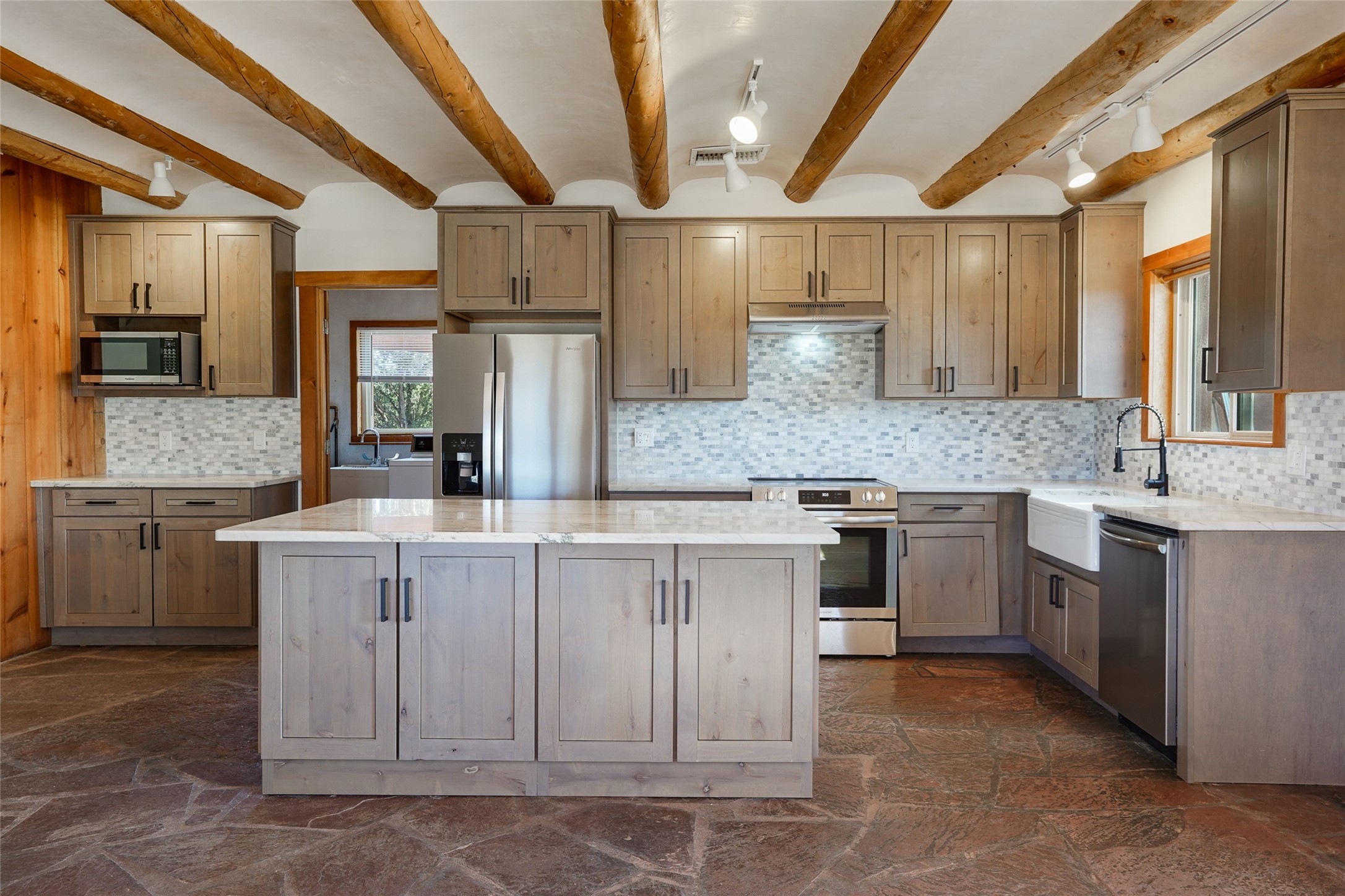 Kitchen with exposed timber ceiling beams, a large stone-topped island, and a white farmhouse sink.