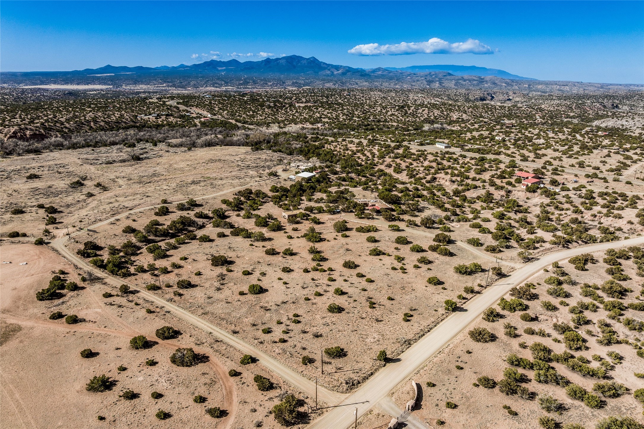 Aerial view of vacant, scrub-covered land bordered by roads, with distant mountains.