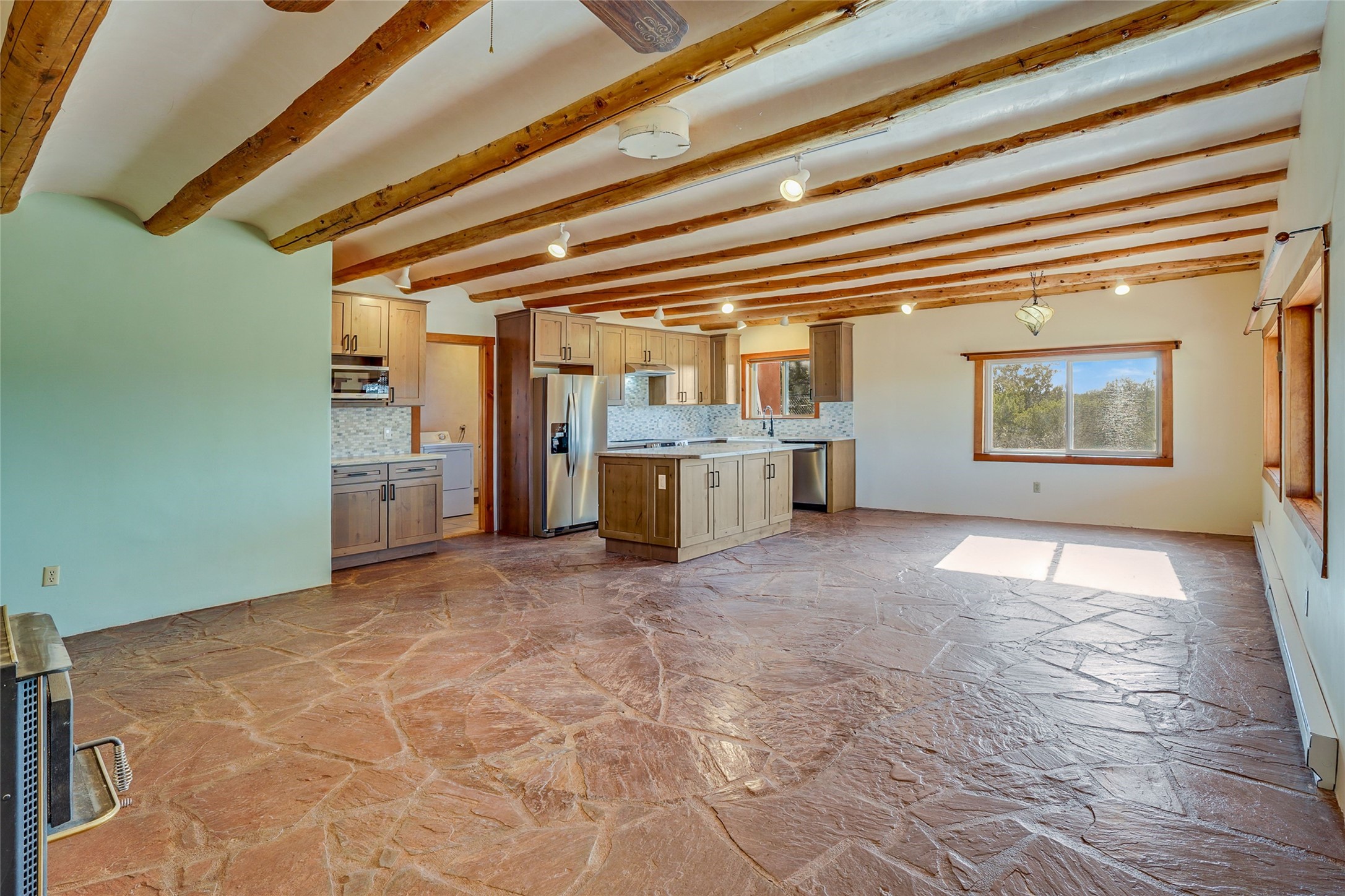 Open kitchen and living area with exposed wood beams, a central island, and flagstone flooring.