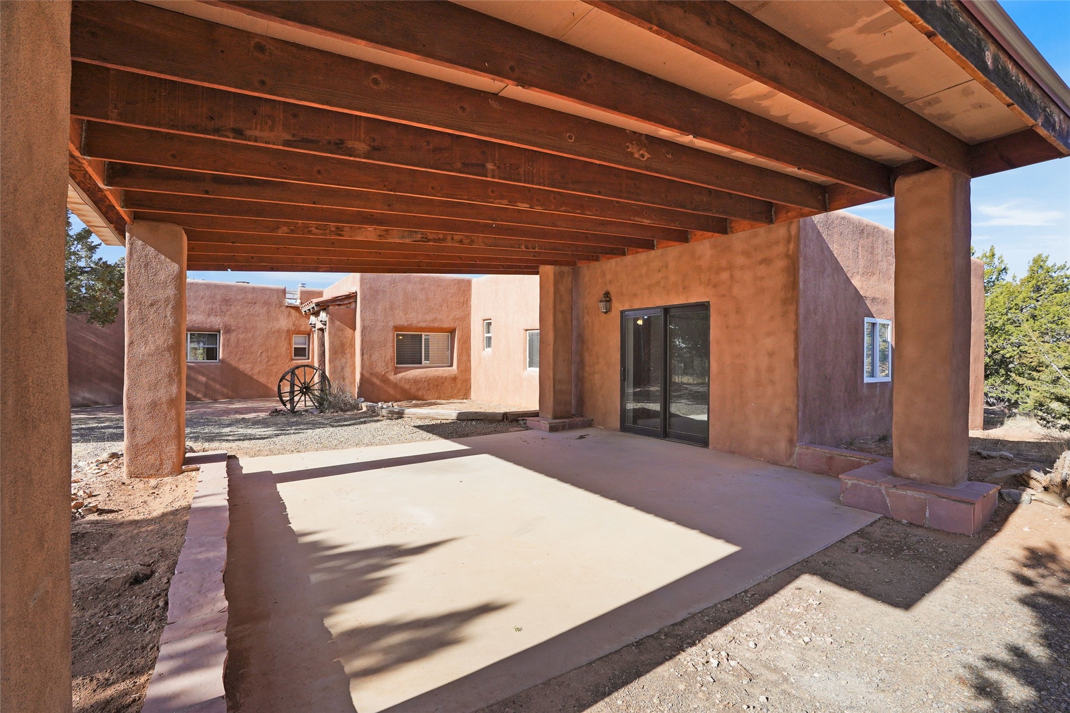 Adobe-style home’s covered patio with exposed wooden beams, stucco columns, and sliding glass doors.