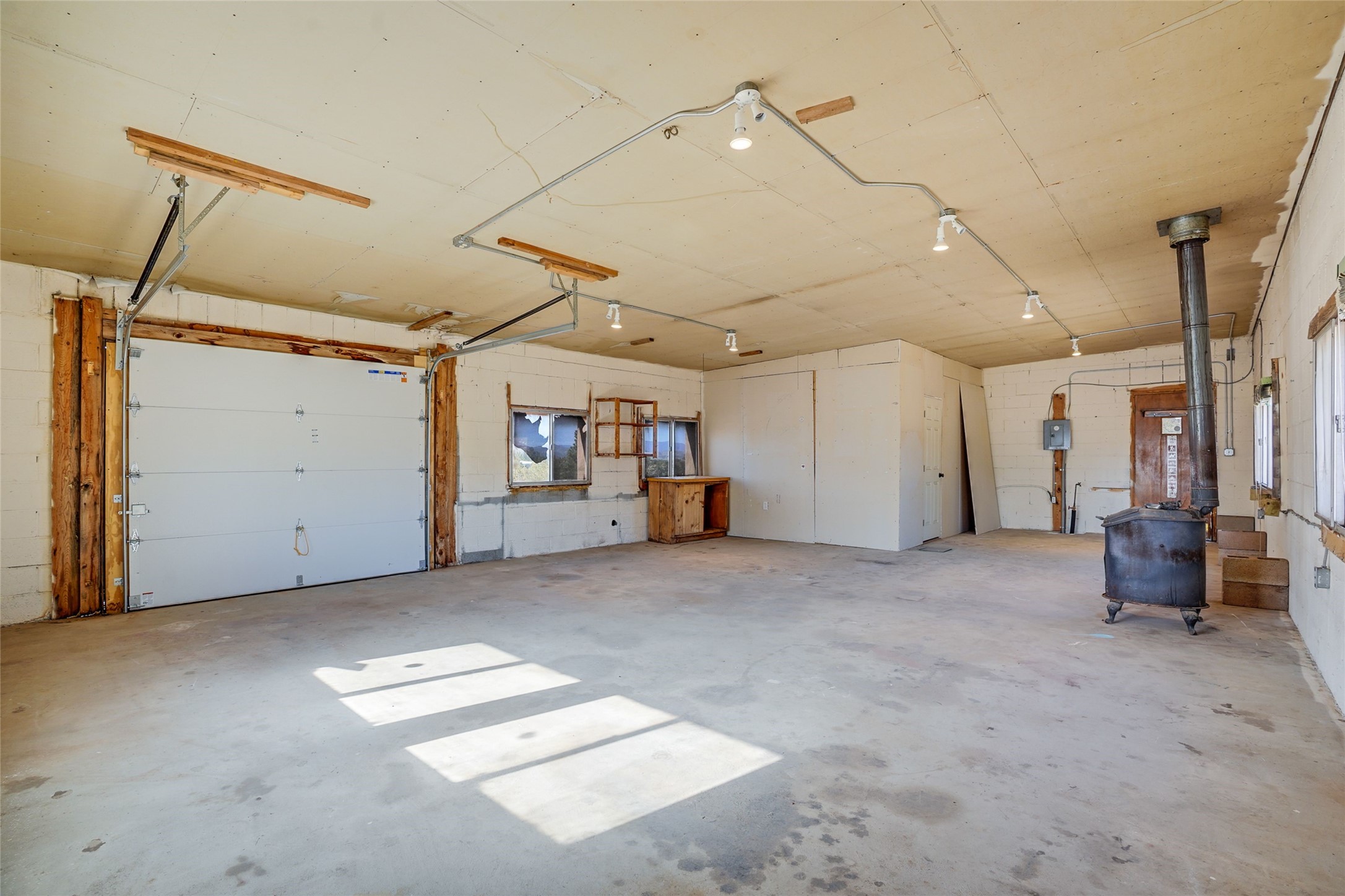 Empty garage with a large overhead door, concrete floor, and freestanding wood stove.
