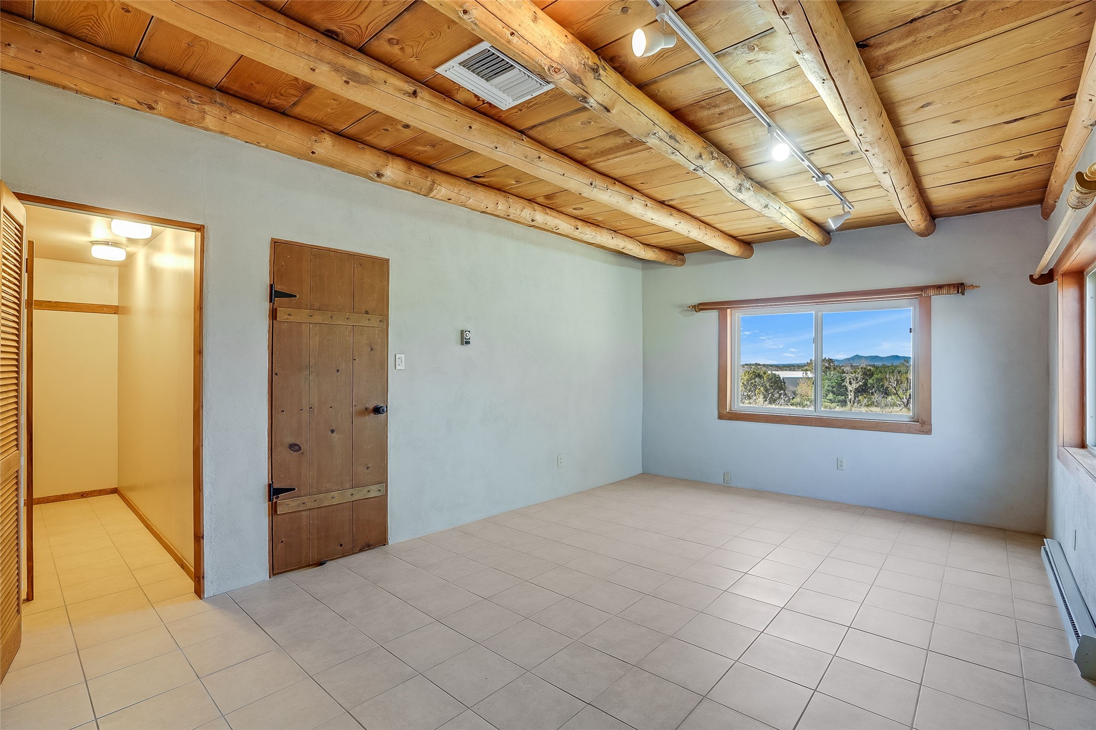 Empty room with exposed timber ceiling, tiled floor, and a window overlooking distant mountains.
