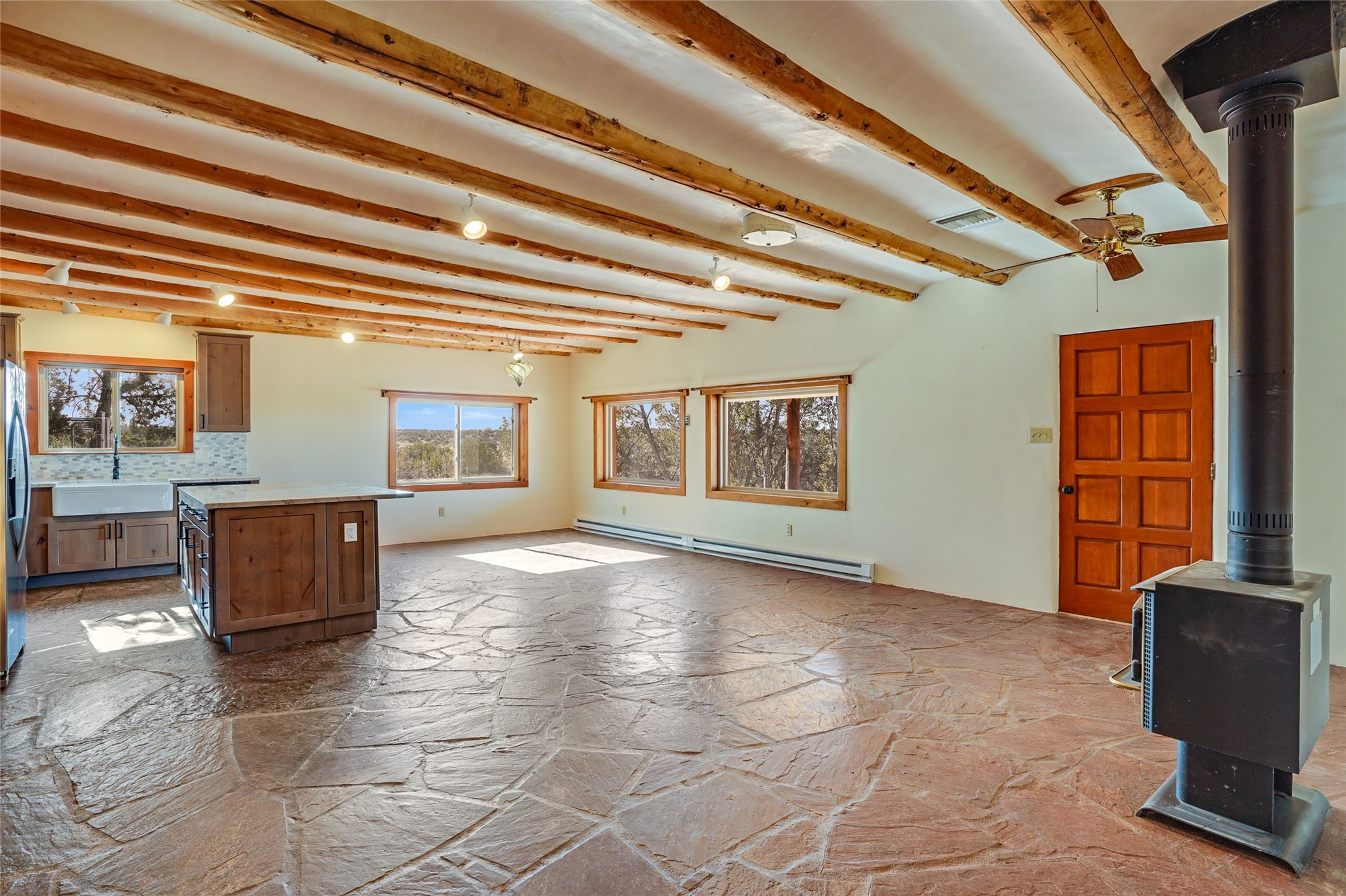 Open kitchen and living area with exposed timber beams, flagstone floors, and a freestanding wood stove.