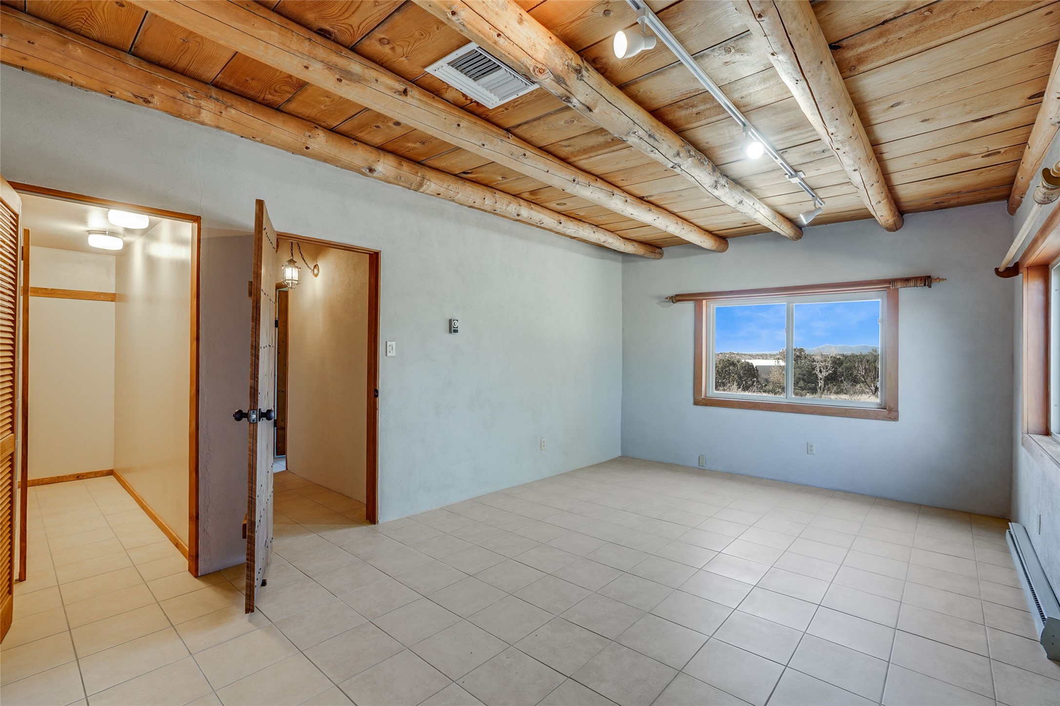 Empty tiled room with exposed wood beams and a window overlooking trees and distant mountains.