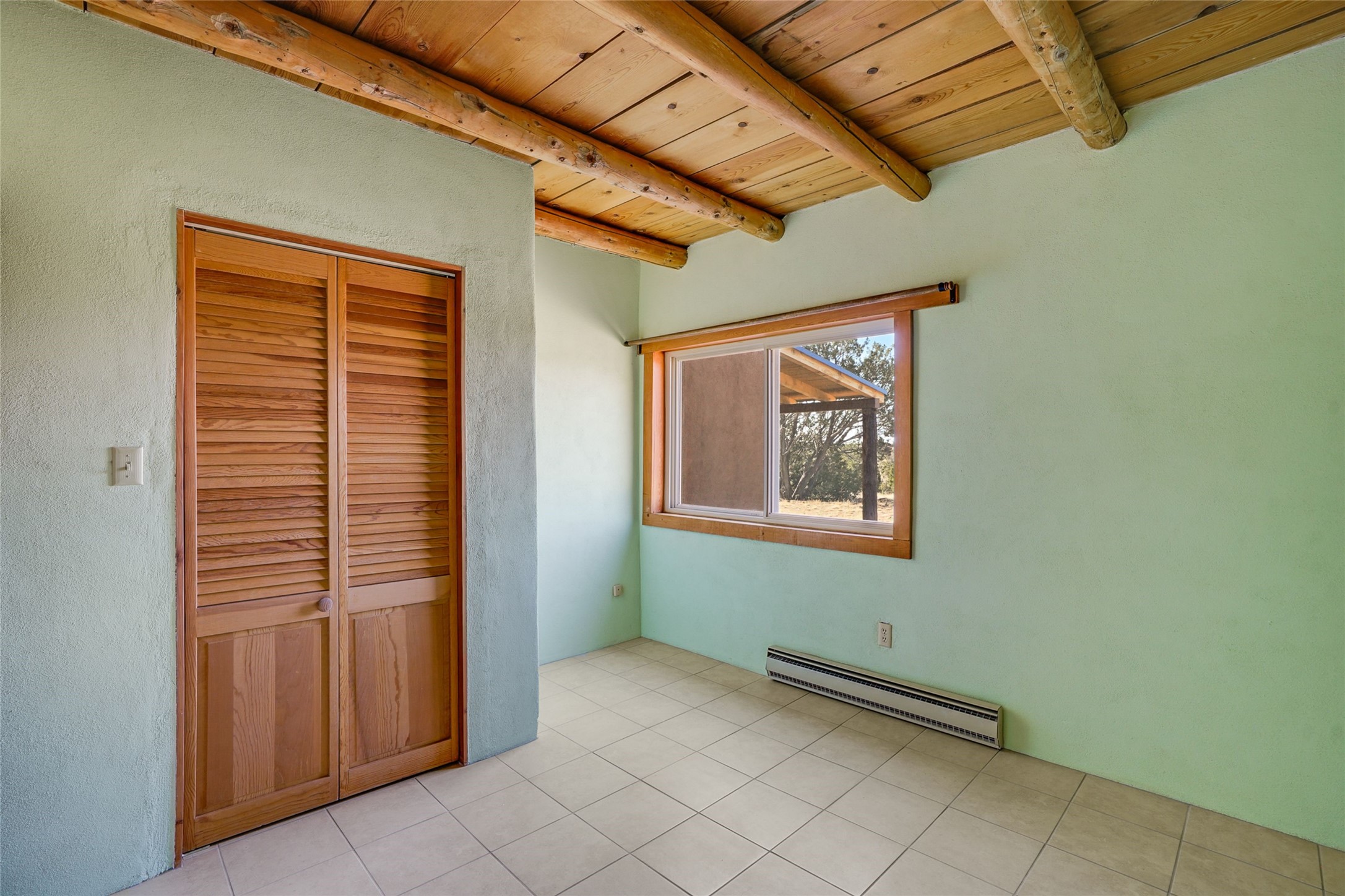 Unfurnished room with wooden louvered closet doors, tiled floor, and exposed wood ceiling beams.