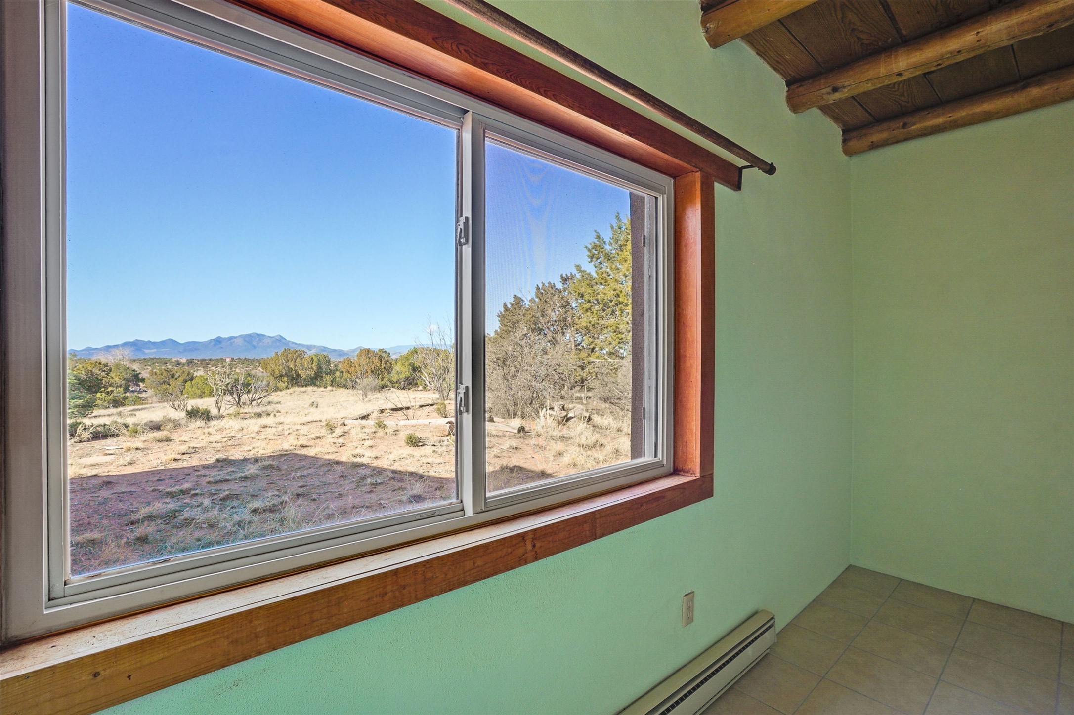Room with a large wood-trimmed window overlooking open land and distant mountains.