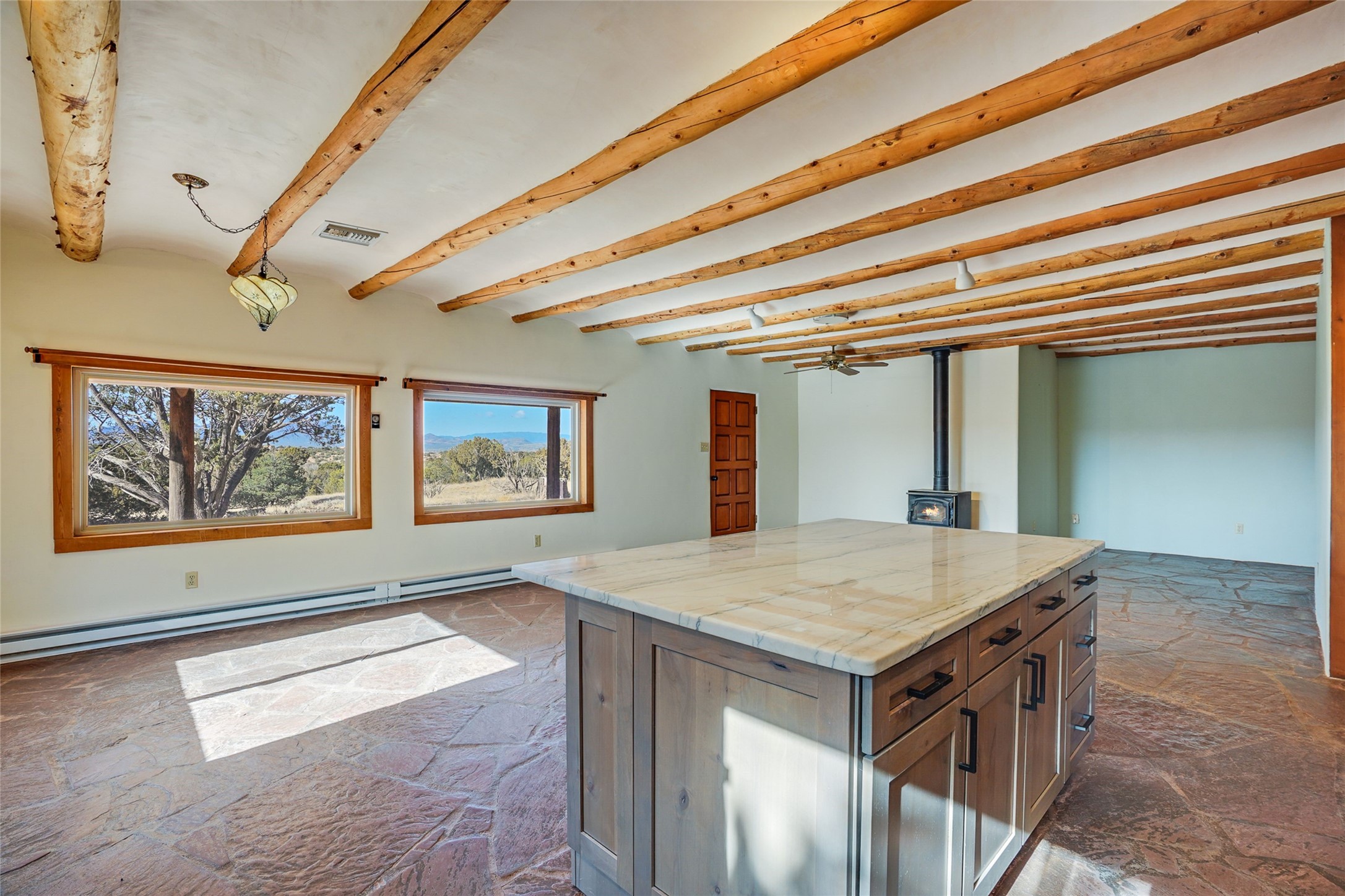 Open kitchen with a large stone-topped island, exposed timber beams, and mountain views through two windows.