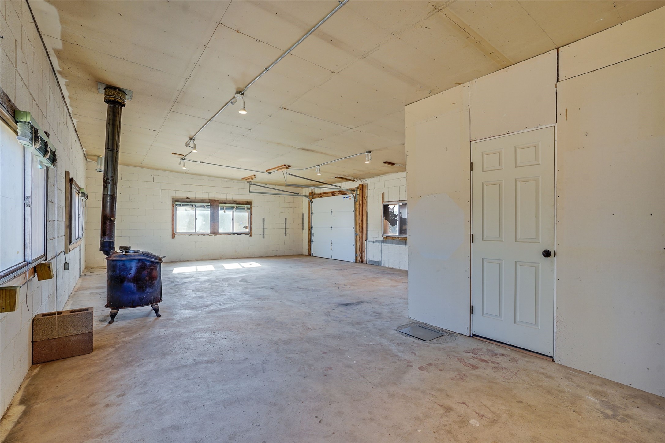 Empty garage with a freestanding wood stove, concrete floor, and overhead garage door.