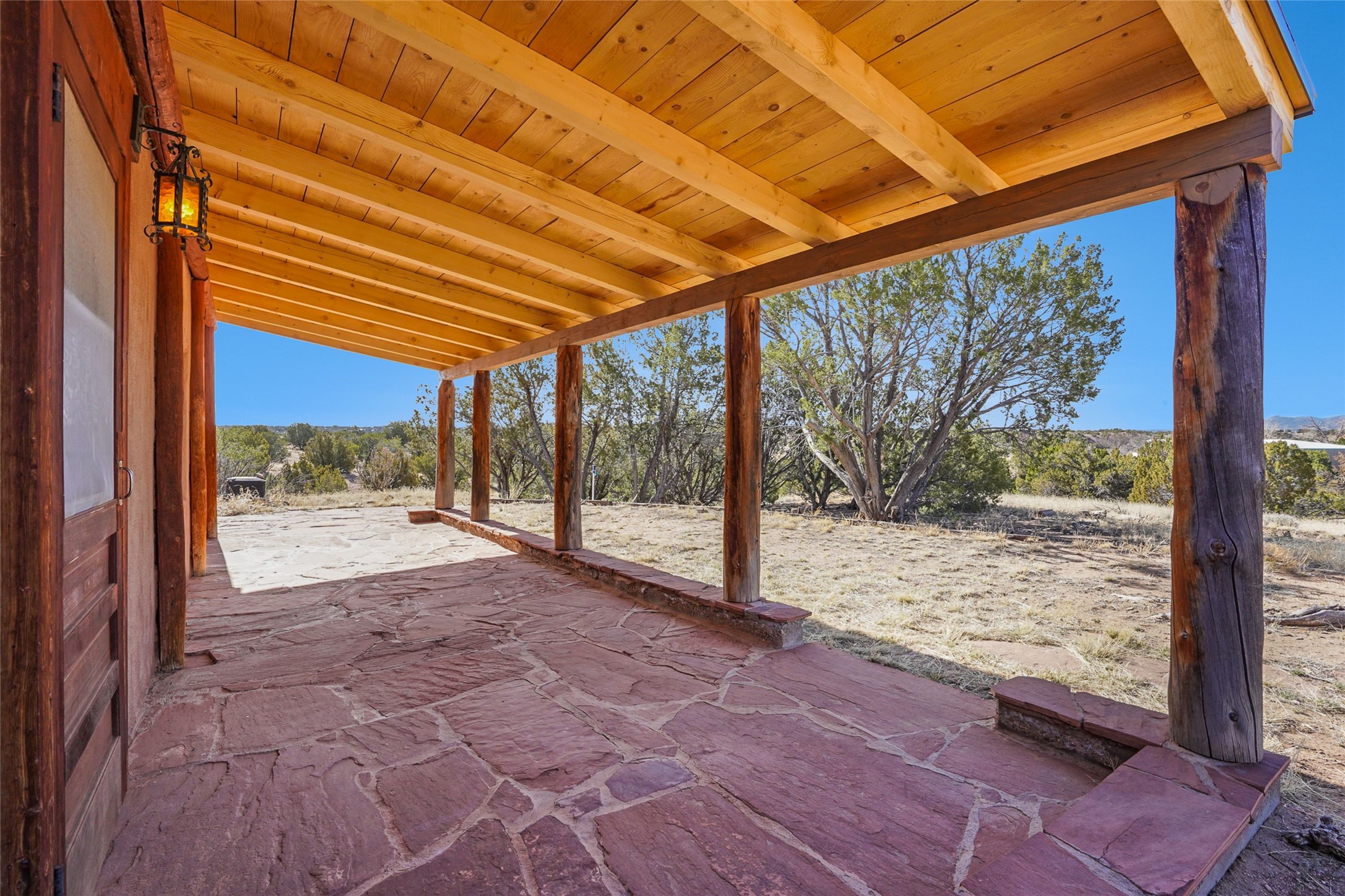 Covered timber porch with a red flagstone floor overlooking trees and distant hills.