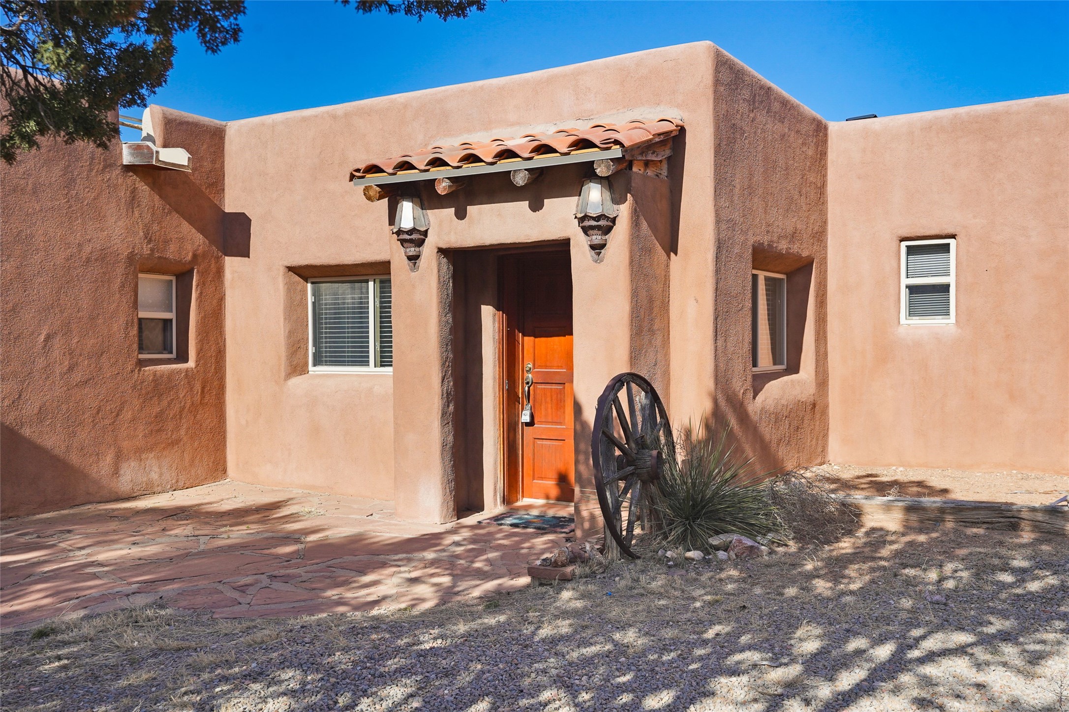 Southwestern stucco home entrance with a terracotta-tiled awning, wooden door, and wagon wheel.