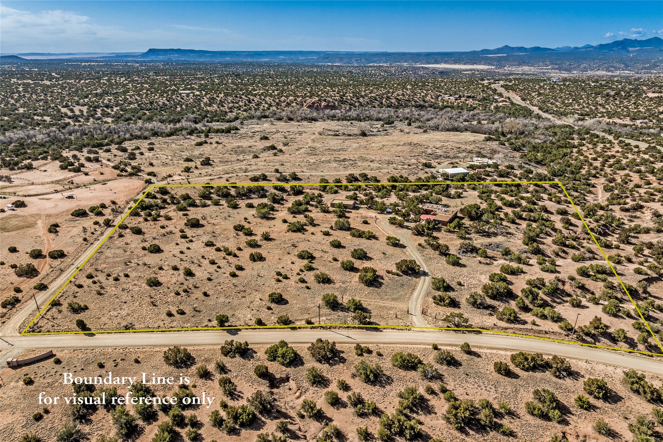 Aerial view of scrub-covered land outlined in yellow, with a dirt road and distant mountains.