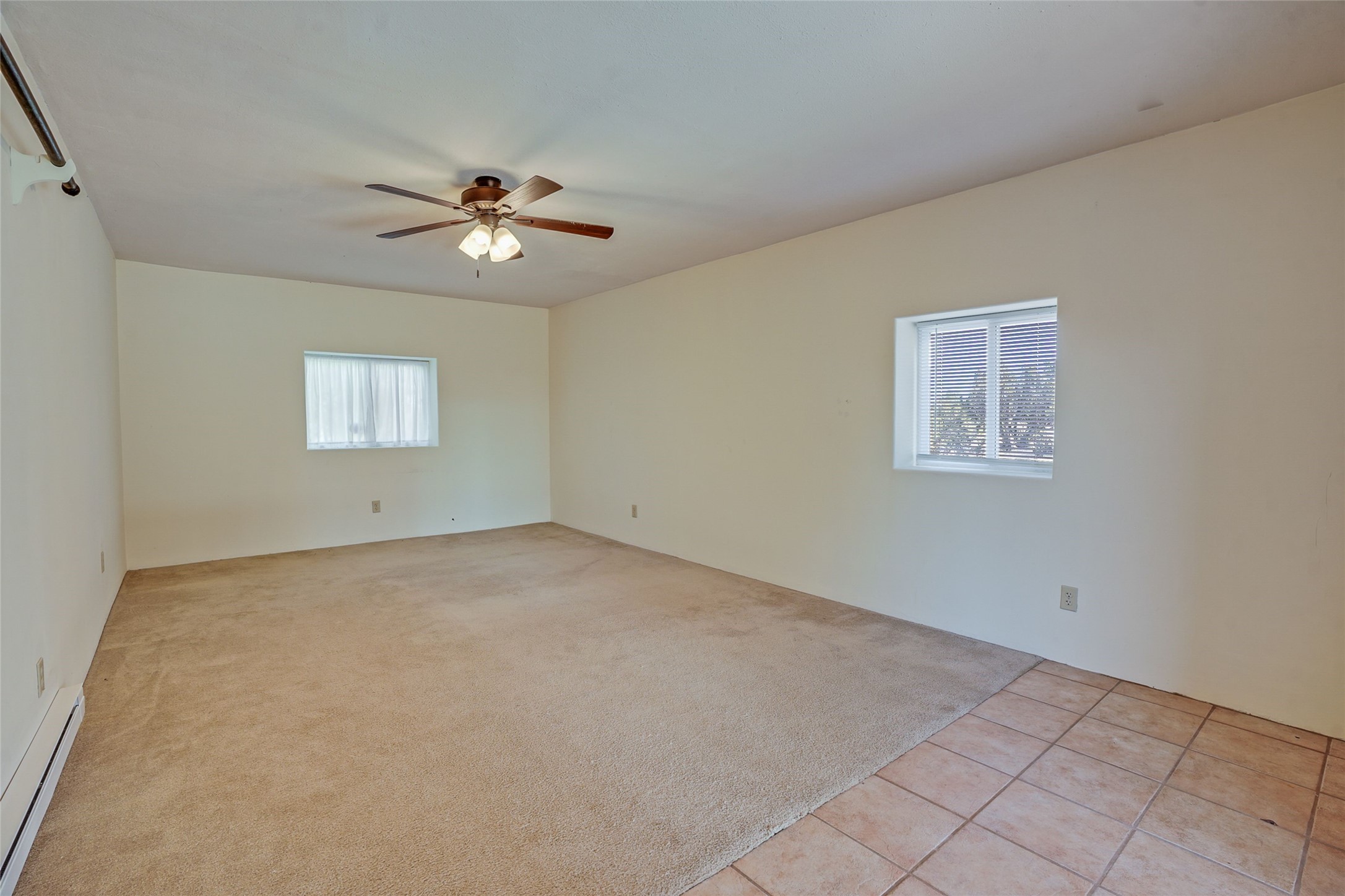 Empty room with beige carpet, terracotta tile flooring, two windows, and a ceiling fan.
