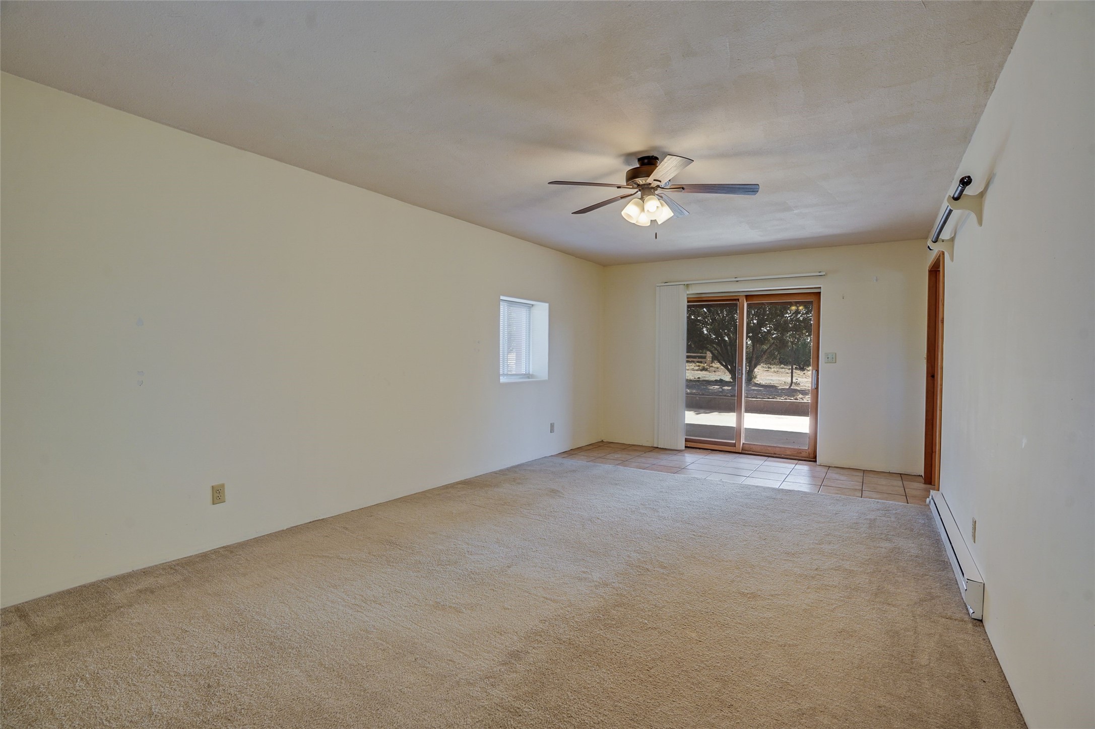 Empty living room with beige carpet, a ceiling fan, and sliding glass doors to a patio.