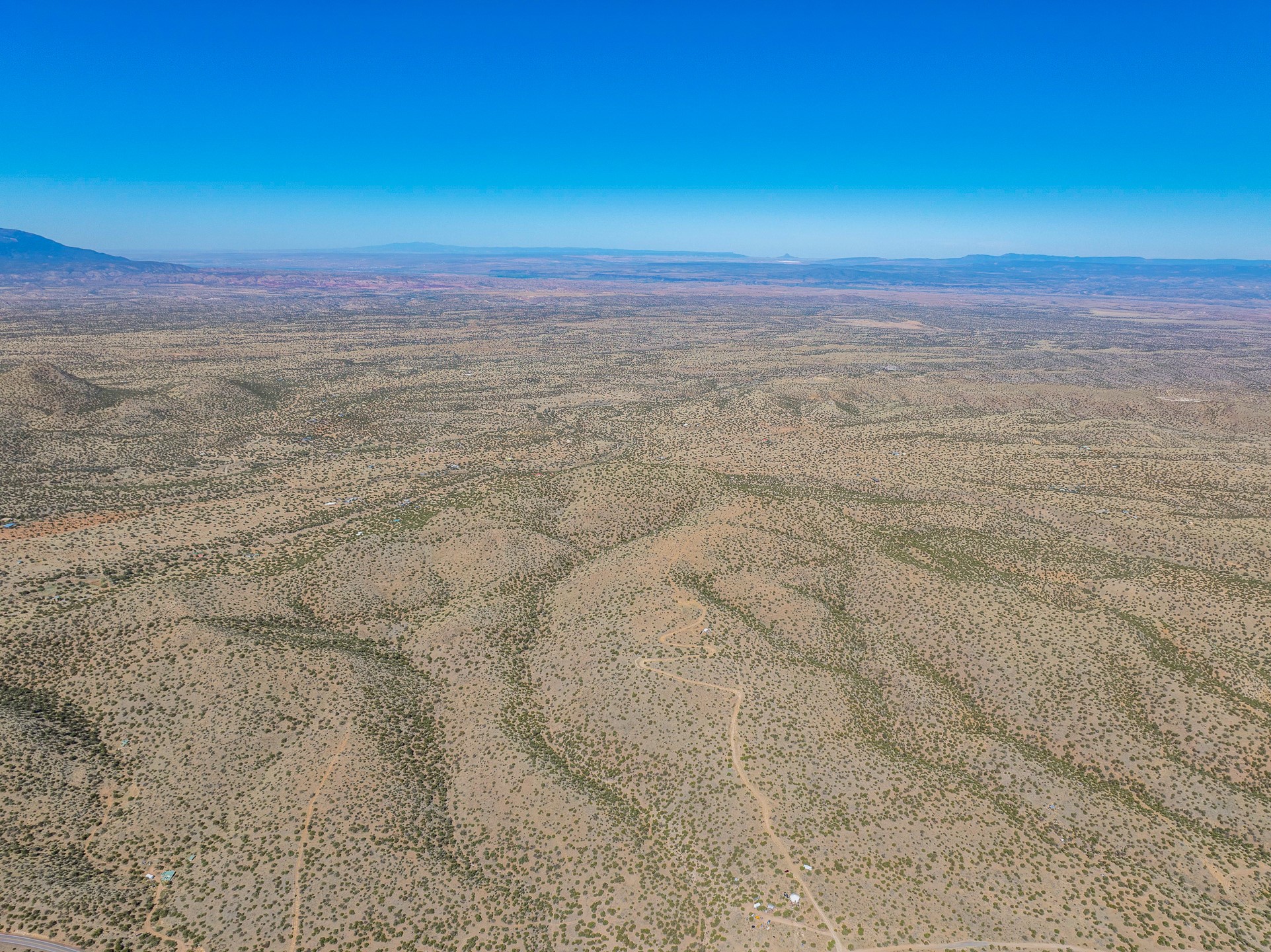 Aerial view of vacant desert land with dirt tracks, a roadside edge, and distant mountains.