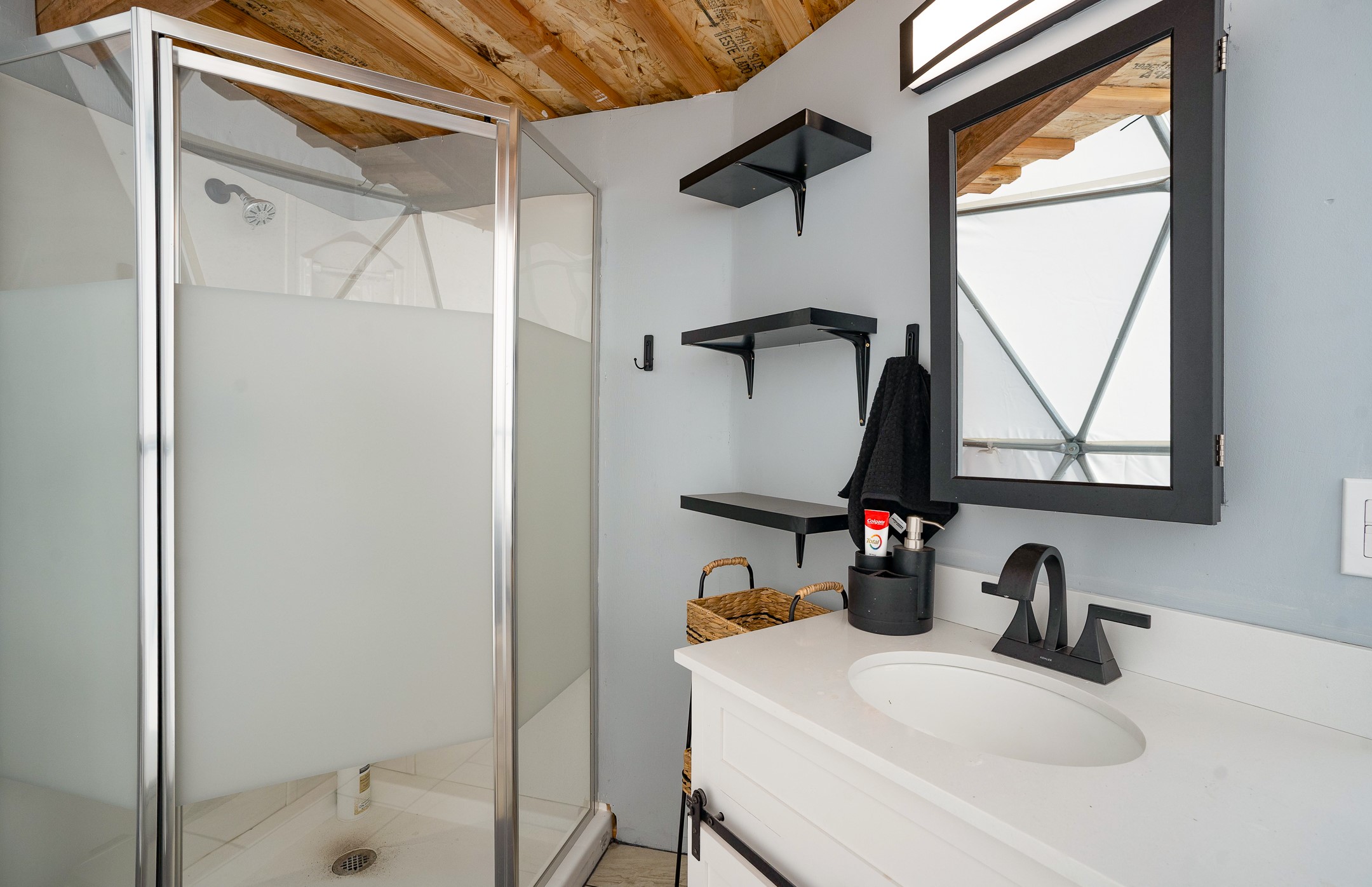 Bathroom with a glass shower, white vanity, black fixtures, and exposed wood ceiling.