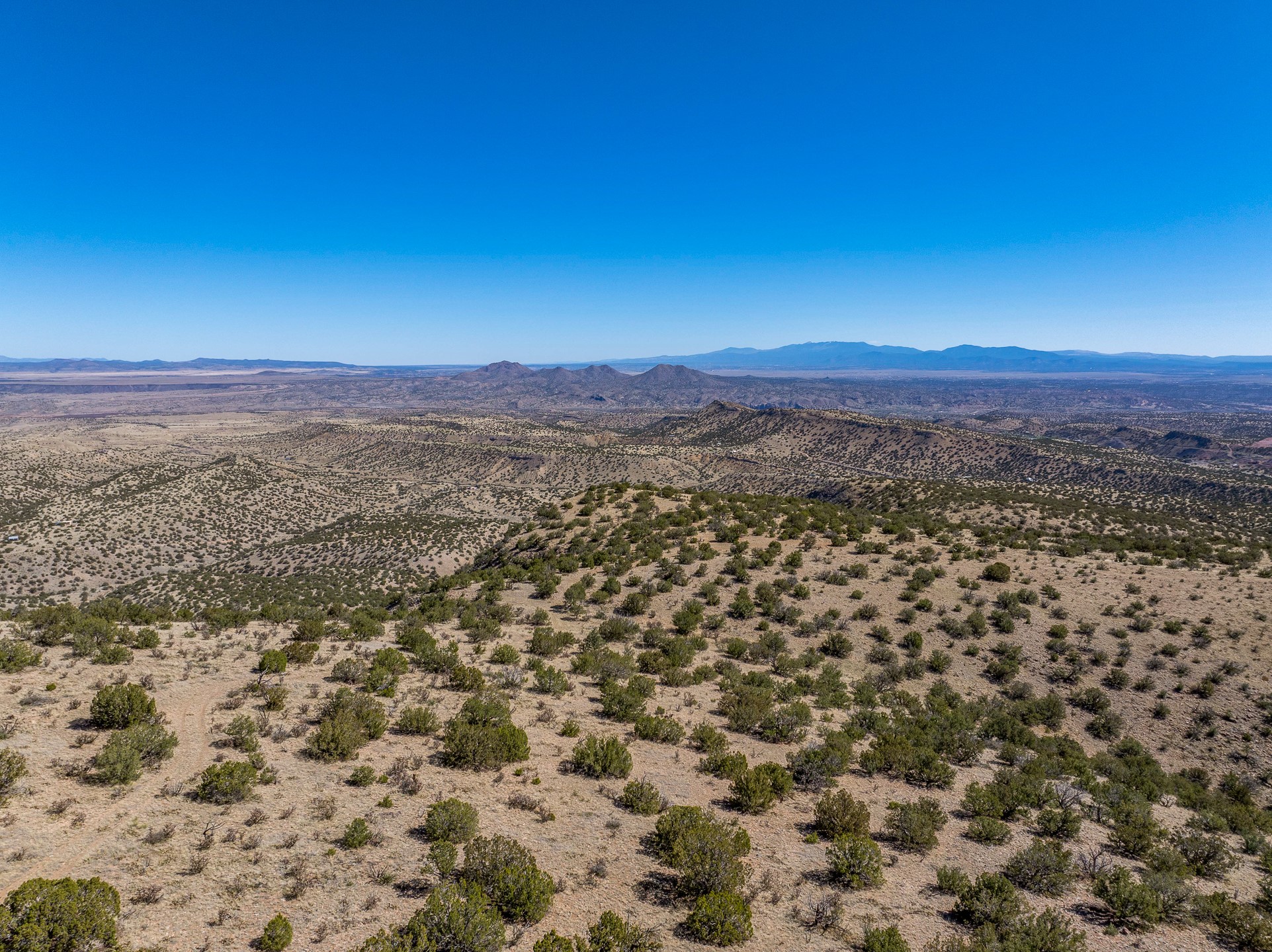 Desert land with scattered scrub overlooks rolling hills and distant mountain ranges.