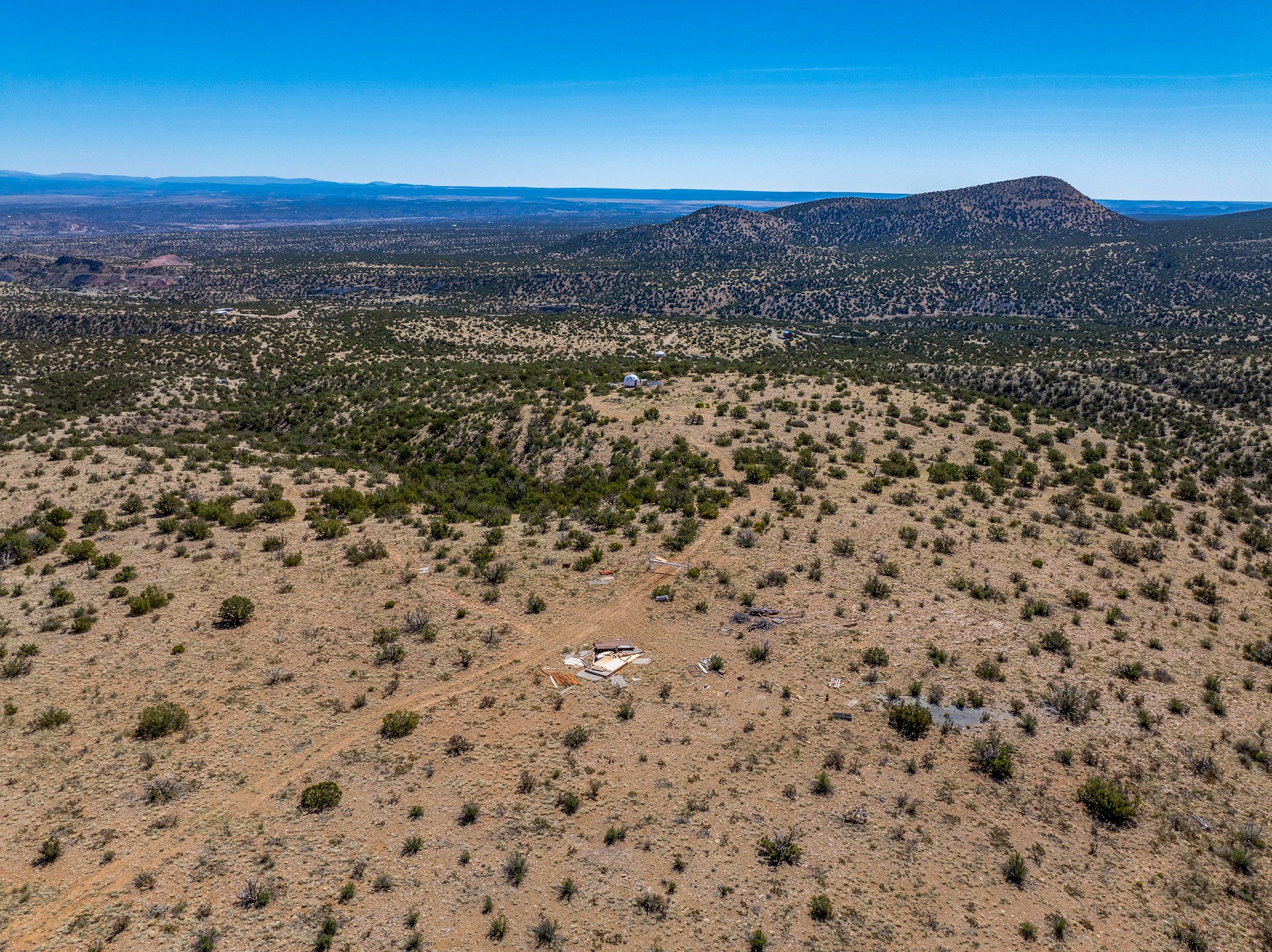 Aerial view of scrub-covered vacant land with a dirt track and distant hills.