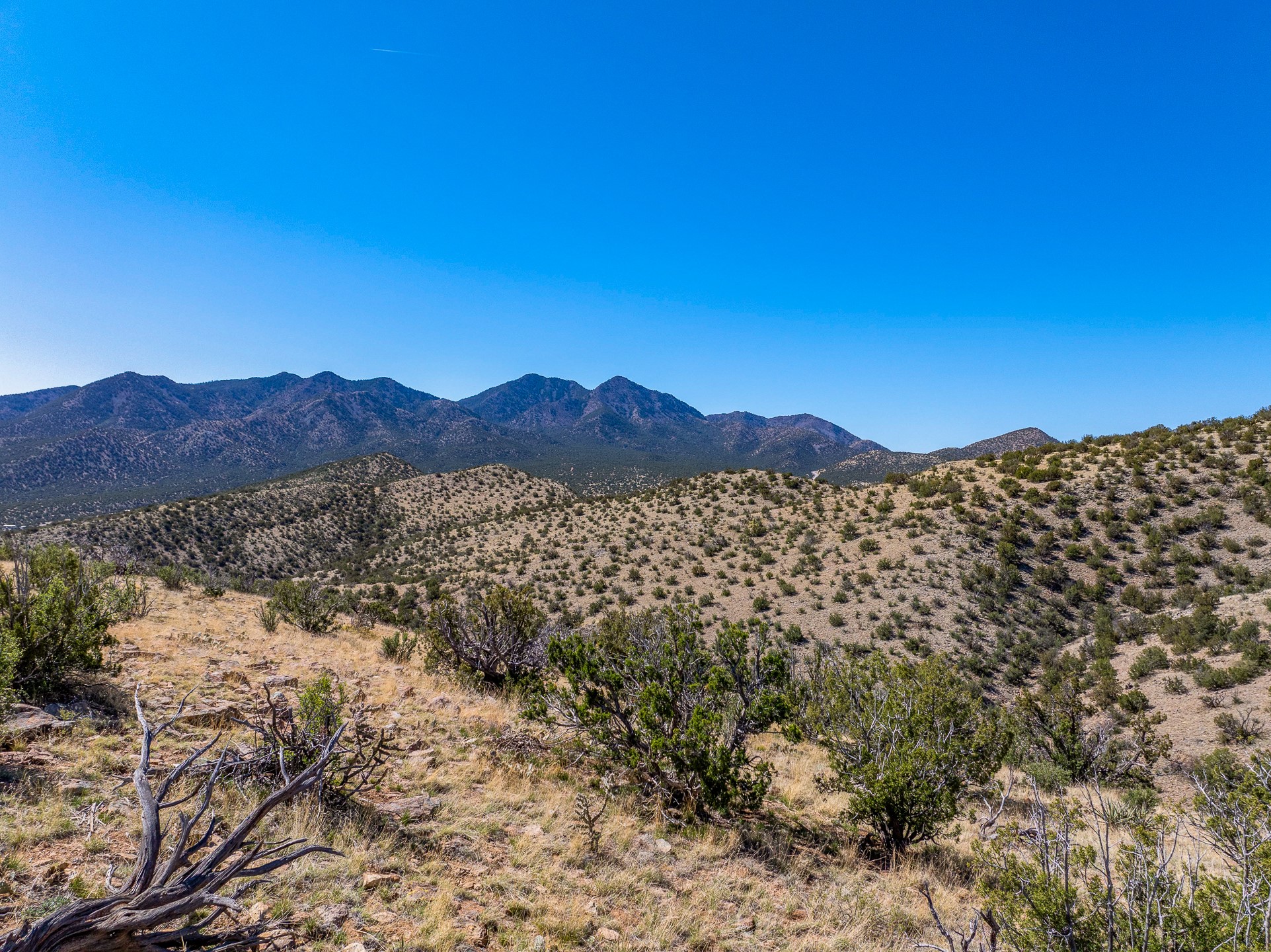 Undeveloped desert land with scrub-covered hills and a rugged mountain range beyond.