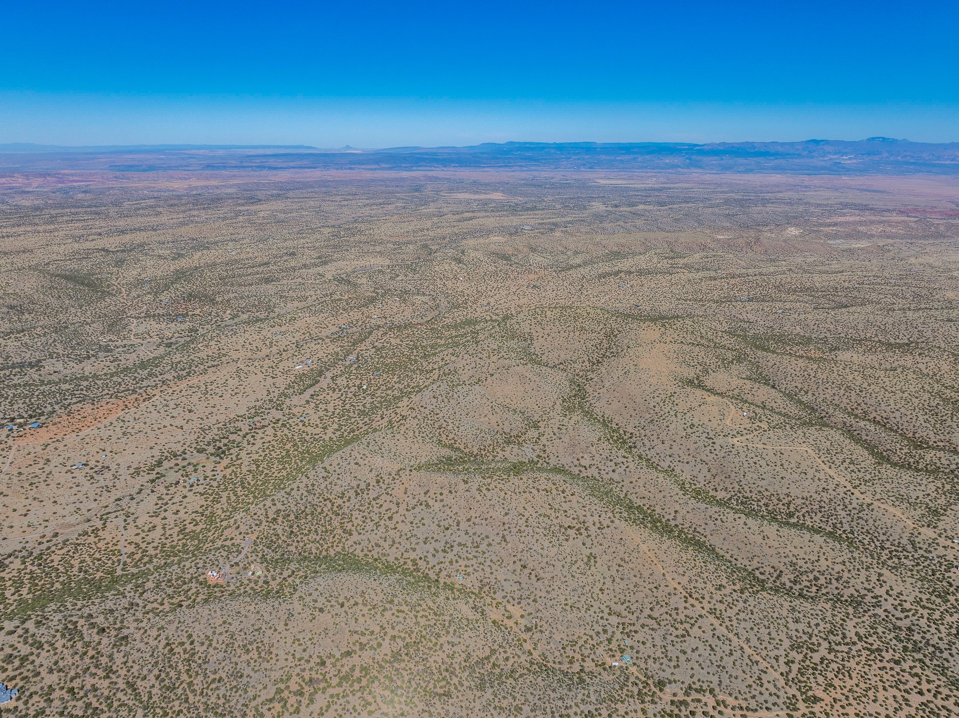 Aerial view of scrub-covered land with scattered buildings, dirt roads, and distant mountains.