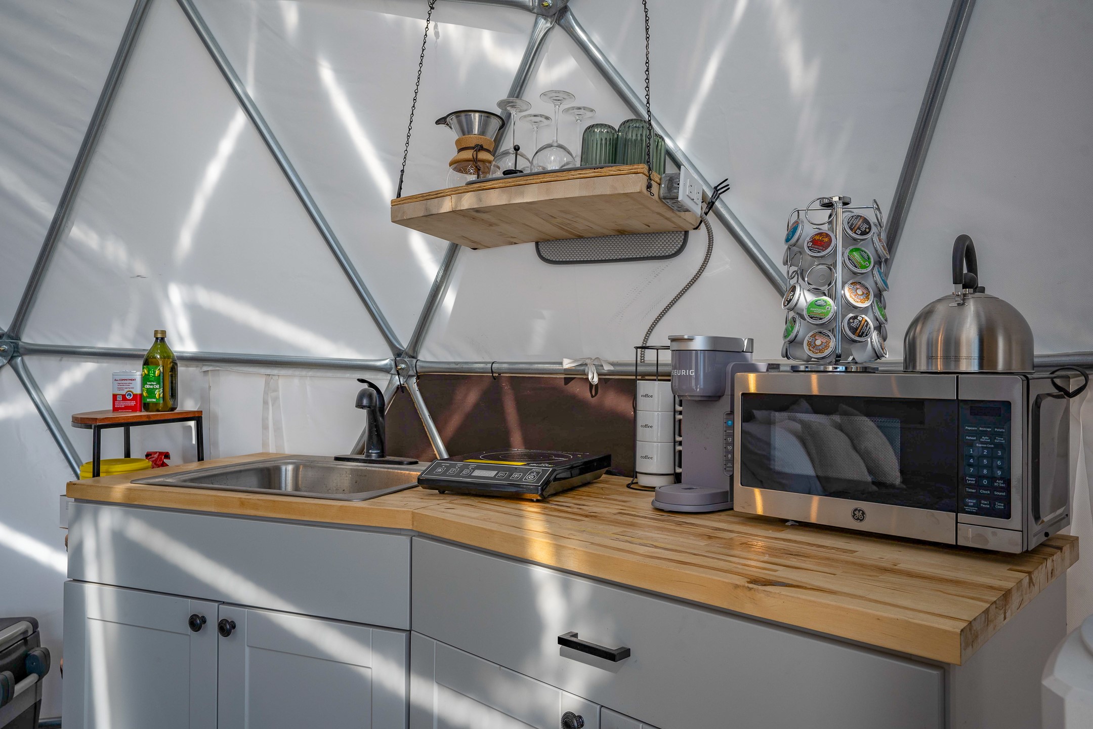 Dome kitchen with a butcher-block counter, stainless sink, induction cooktop, and microwave.