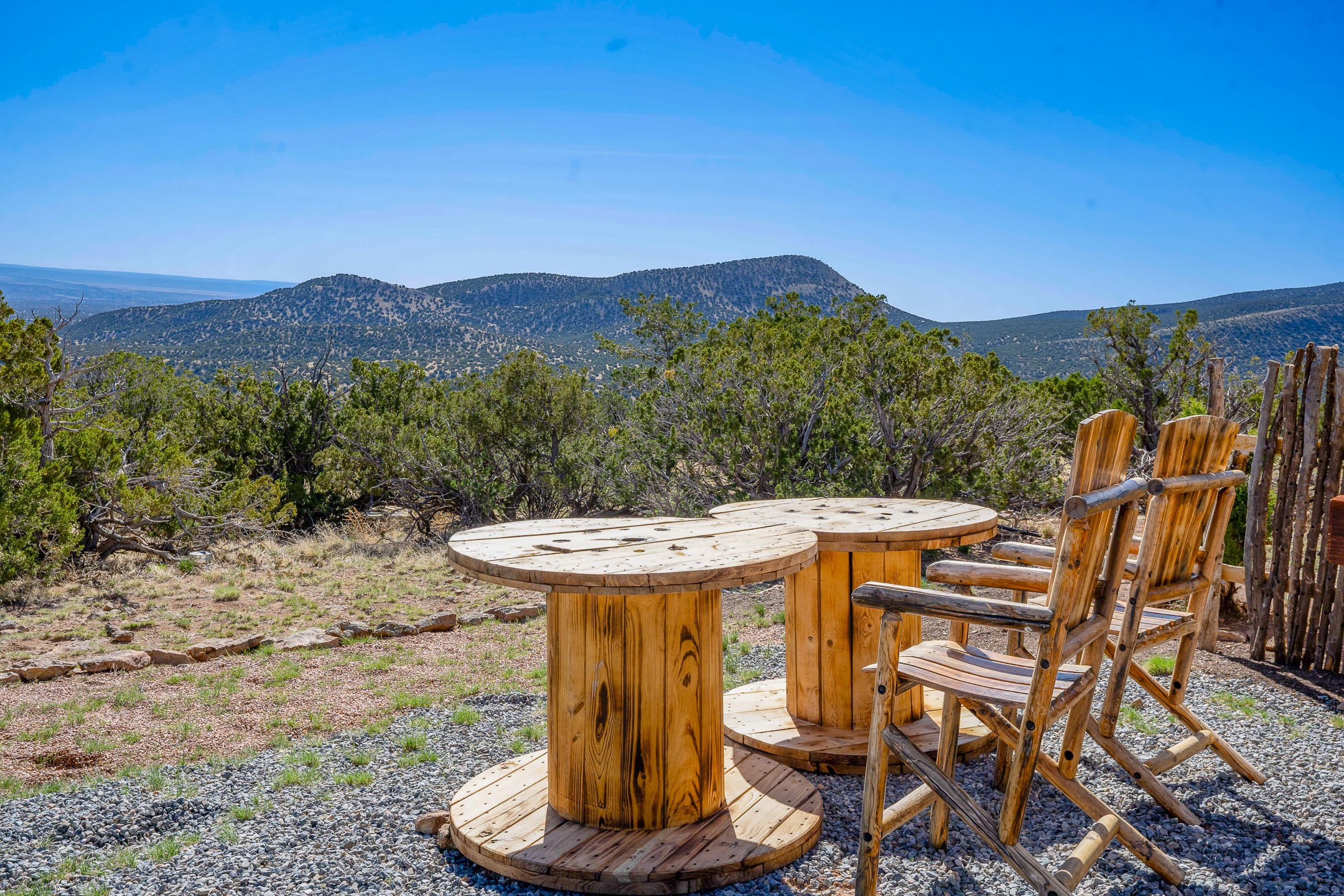 Outdoor wooden tables and chairs overlook scrub-covered hills and distant mountains.